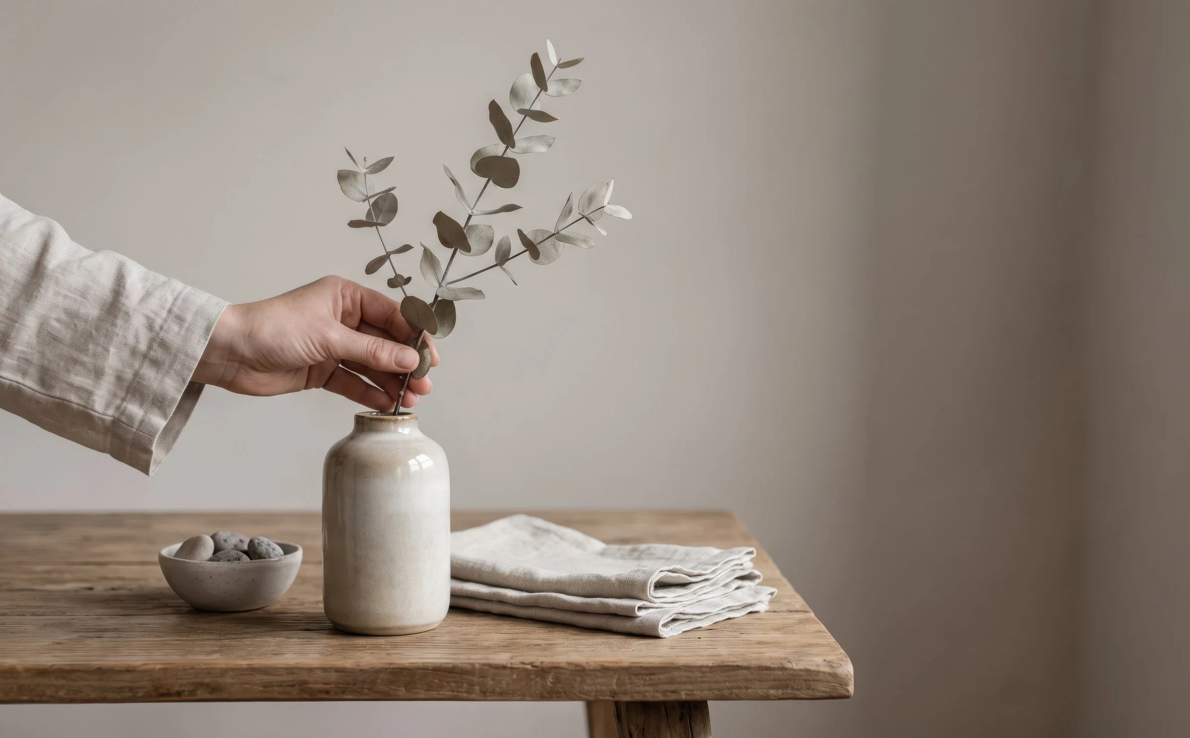 Hand placing a eucalyptus branch in a ceramic vase on a wooden table