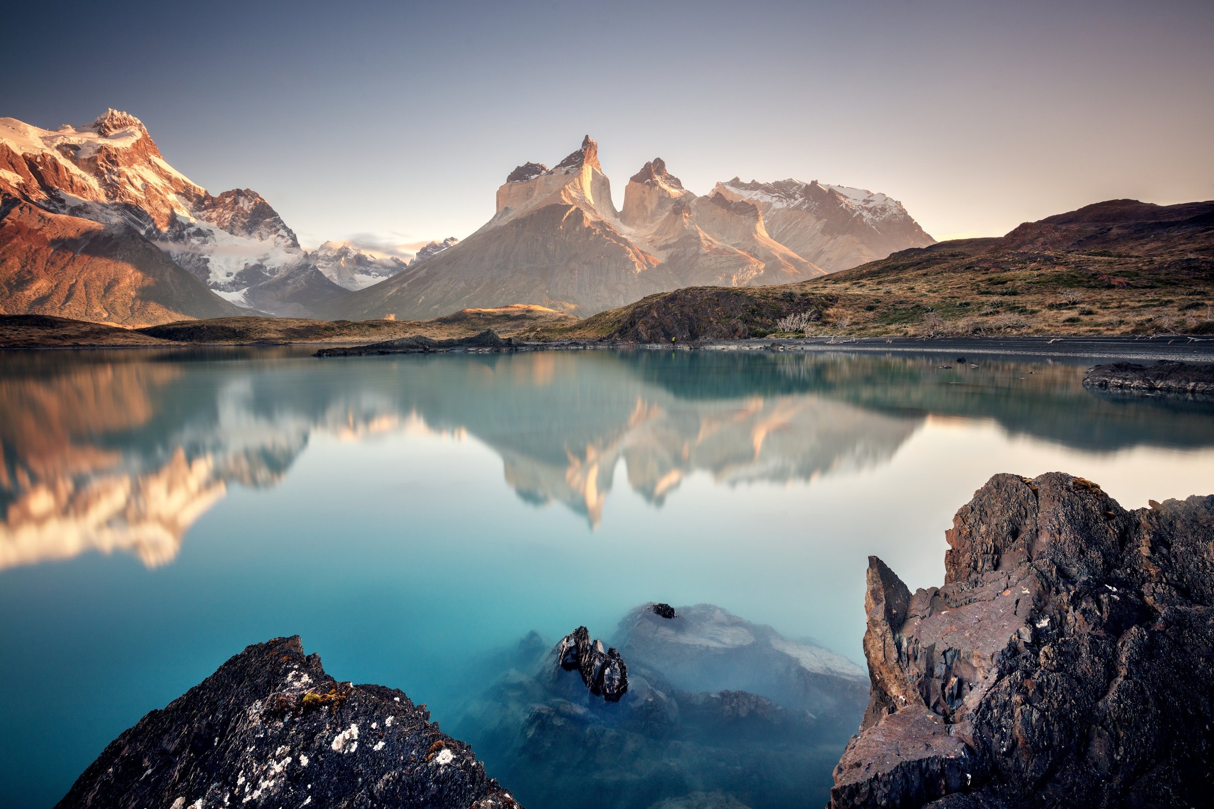 Snow-capped mountain peaks reflected in a calm turquoise lake at sunrise
