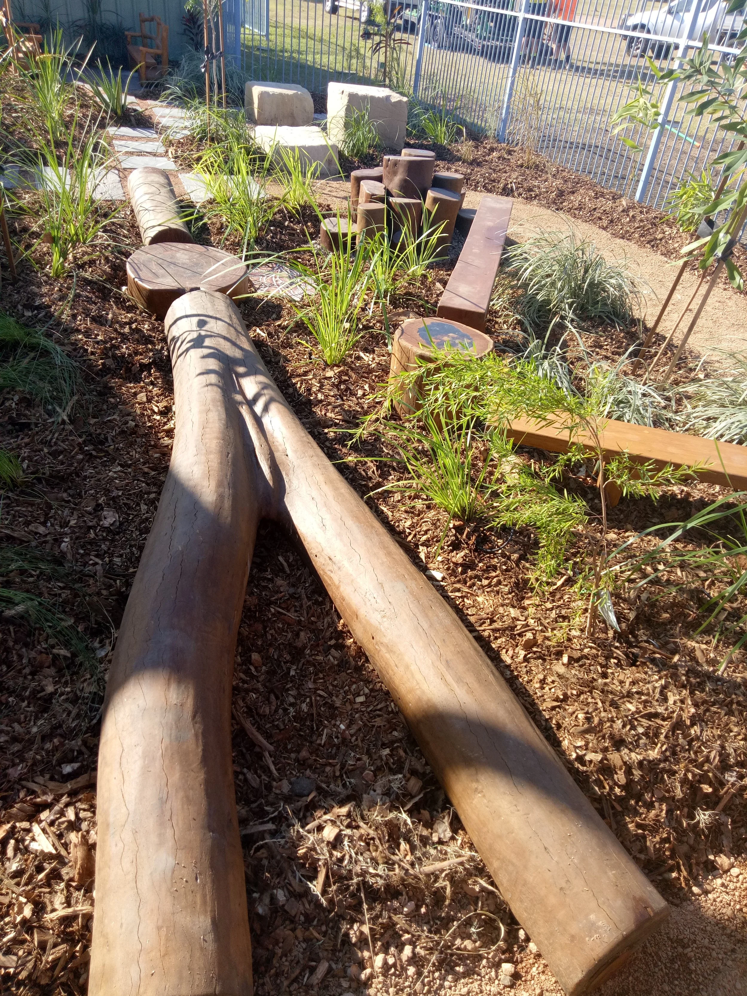 Wooden logs and stumps used as seating and decorations in a garden area, with plants and gravel surrounding them.