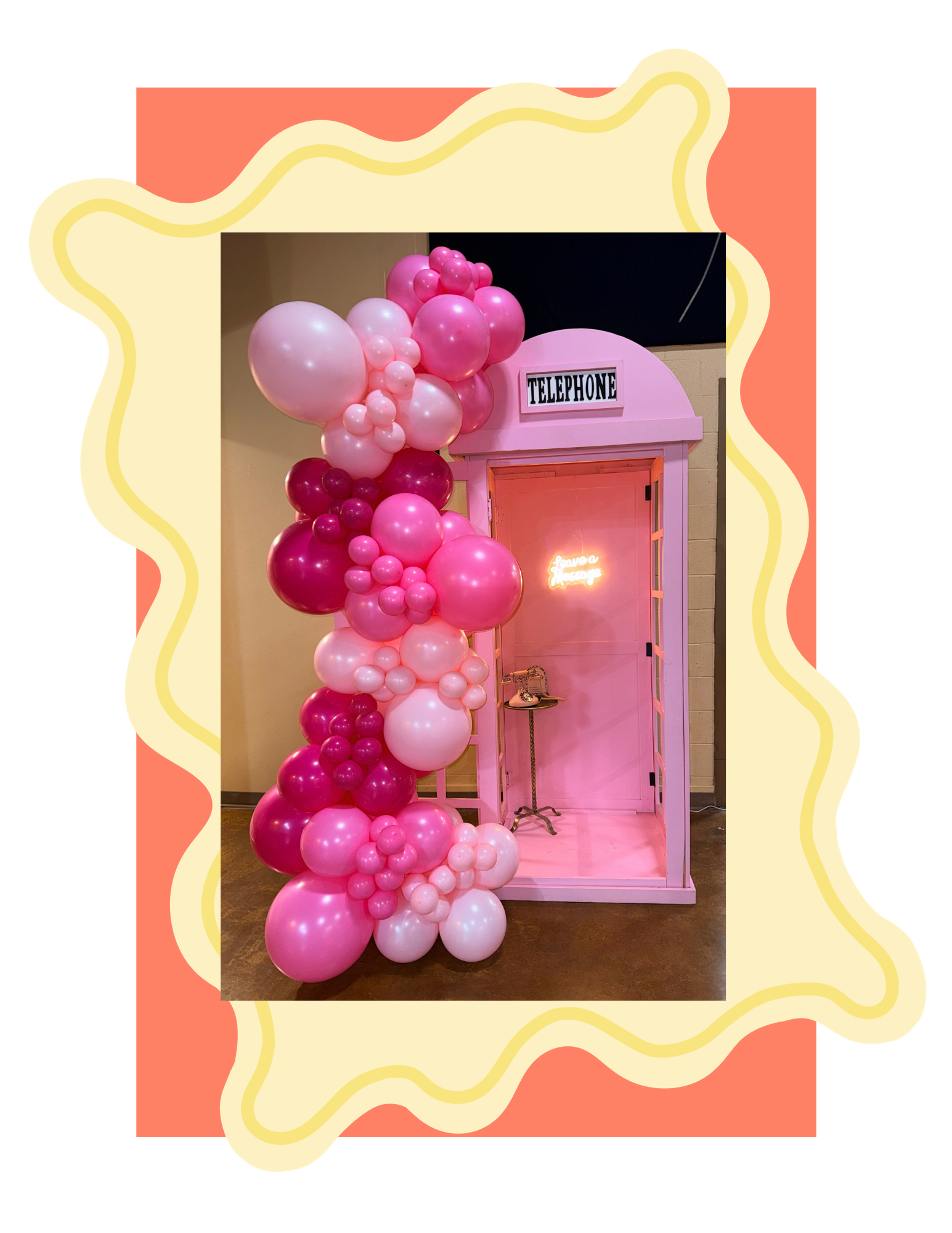 Pink and white balloons arranged around a pink telephone booth with a neon sign inside that says "leave a message."