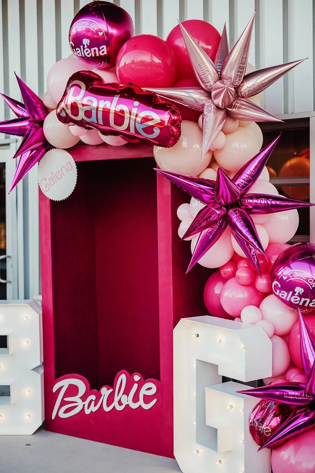 Pink and white balloons arranged around a pink box with a Barbie sign, decorated with shiny star-shaped balloons.