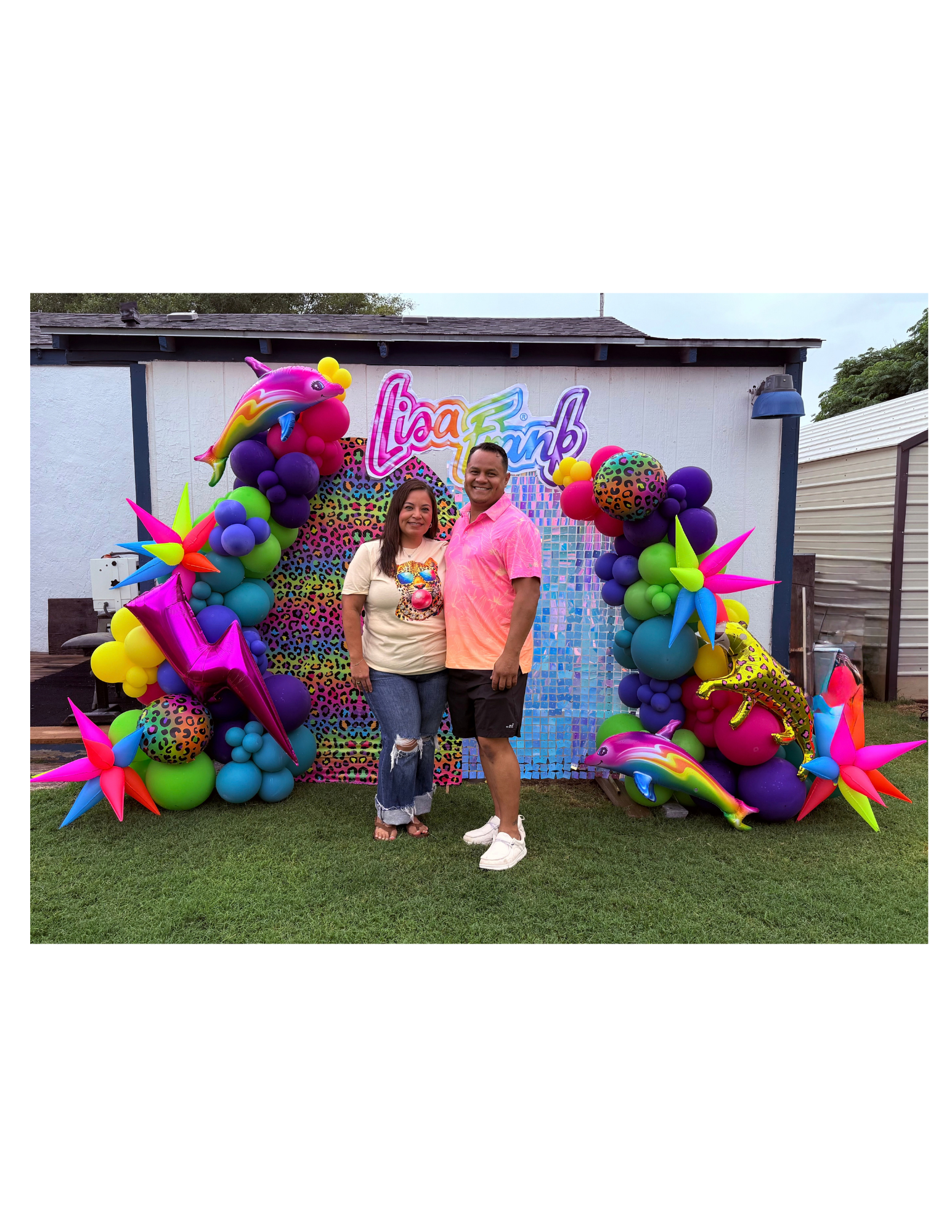 Two people standing and smiling in front of a colorful balloon arch with a 'Lila's 5th' sign, surrounded by balloons shaped like a unicorn, star, and animal print, on a lawn in a backyard.