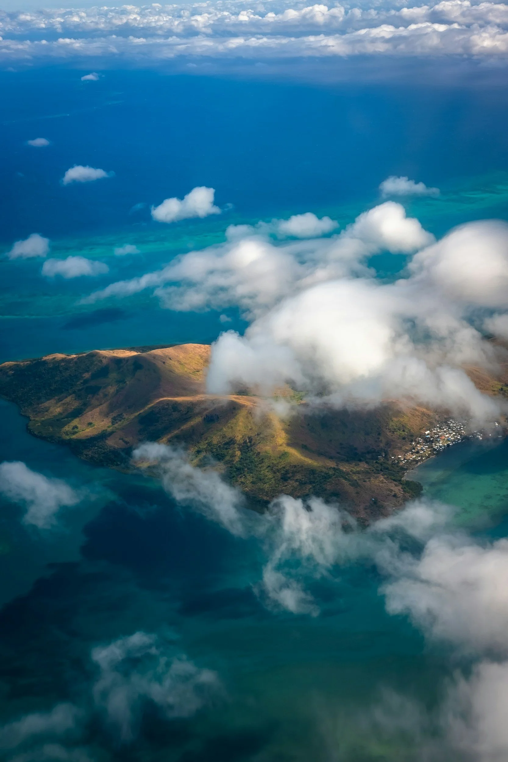Aerial view of a mountainous island in Fiji surrounded by turquoise ocean with clouds overhead.