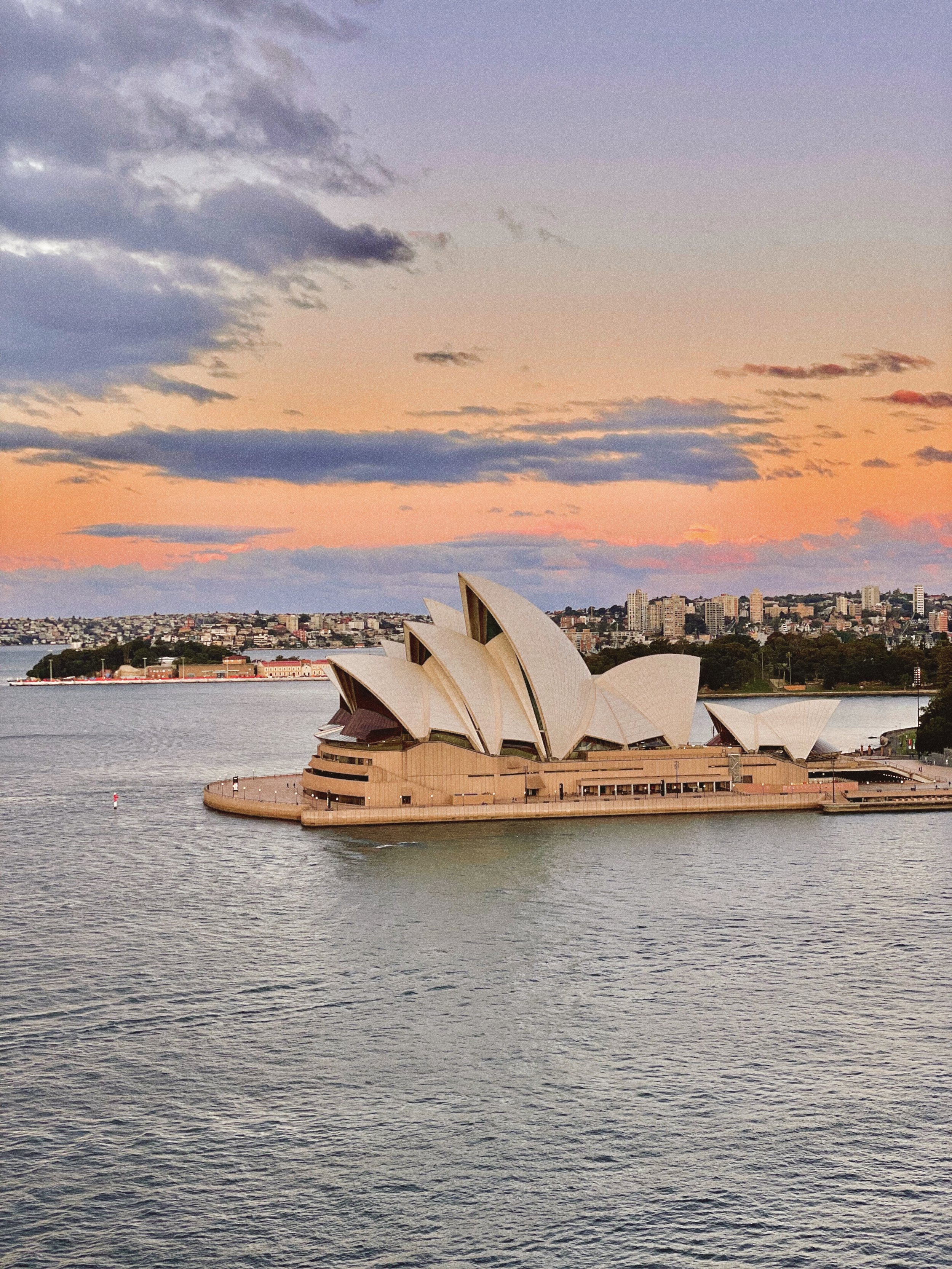 Sydney Opera House during sunset with colorful sky and city skyline in the background.