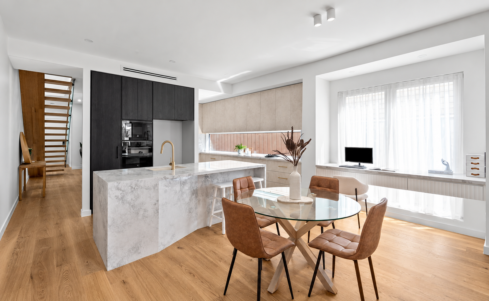 Modern open-concept kitchen and dining area with a marble island, brown leather chairs around a glass table, and a window with sheer curtains