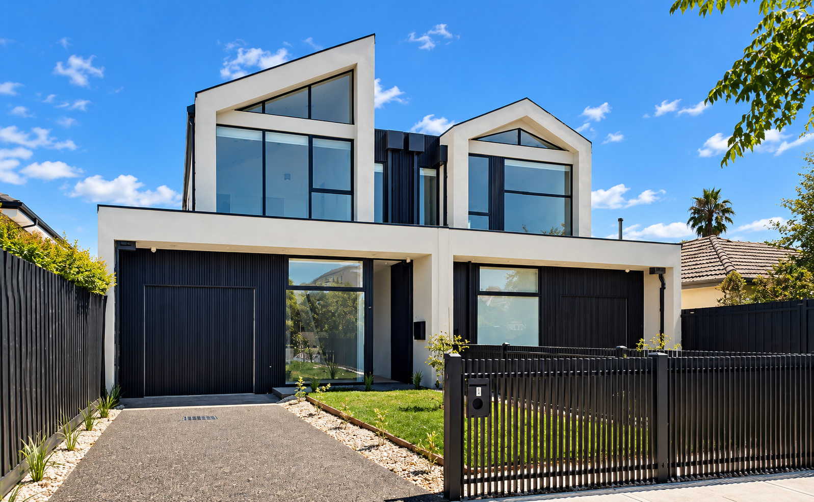 Modern two-story house with white walls, large glass windows, black accents, a lawn, and a black fence, under a blue sky with some clouds.