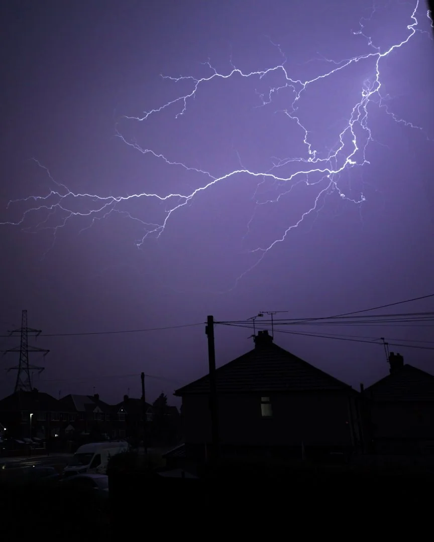 Night sky illuminated by multiple lightning strikes over houses and power lines.