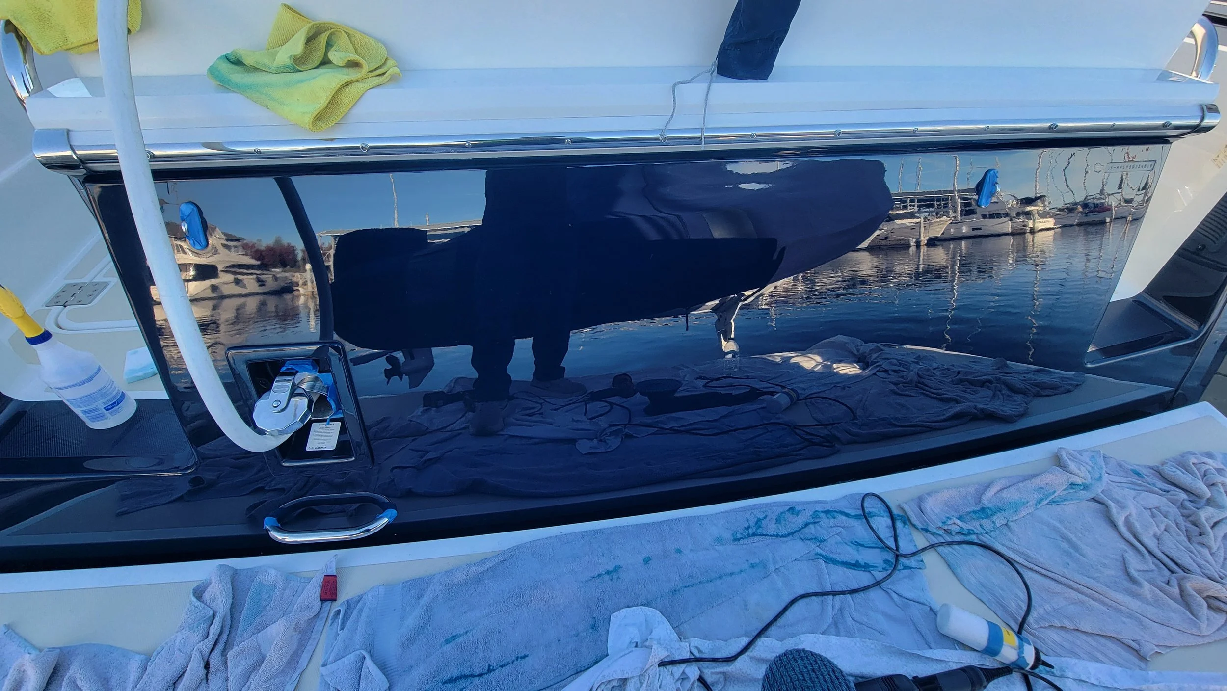 Boat deck with chrome railing, cleaning towels, supplies, and marina reflections on a glossy dark surface