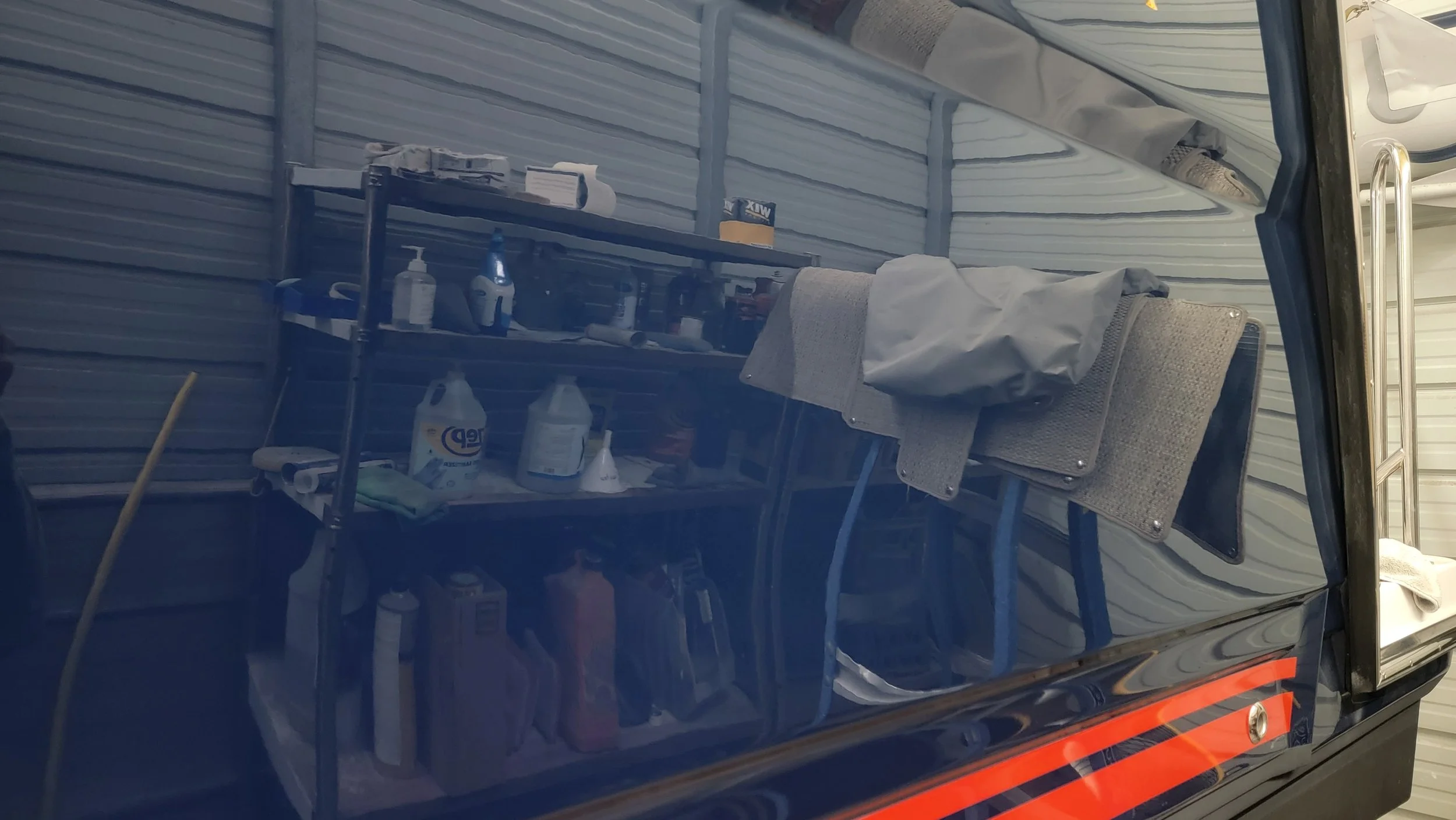 Shelves stocked with cleaning supplies, bottles, towels, and folding chairs inside a storage compartment