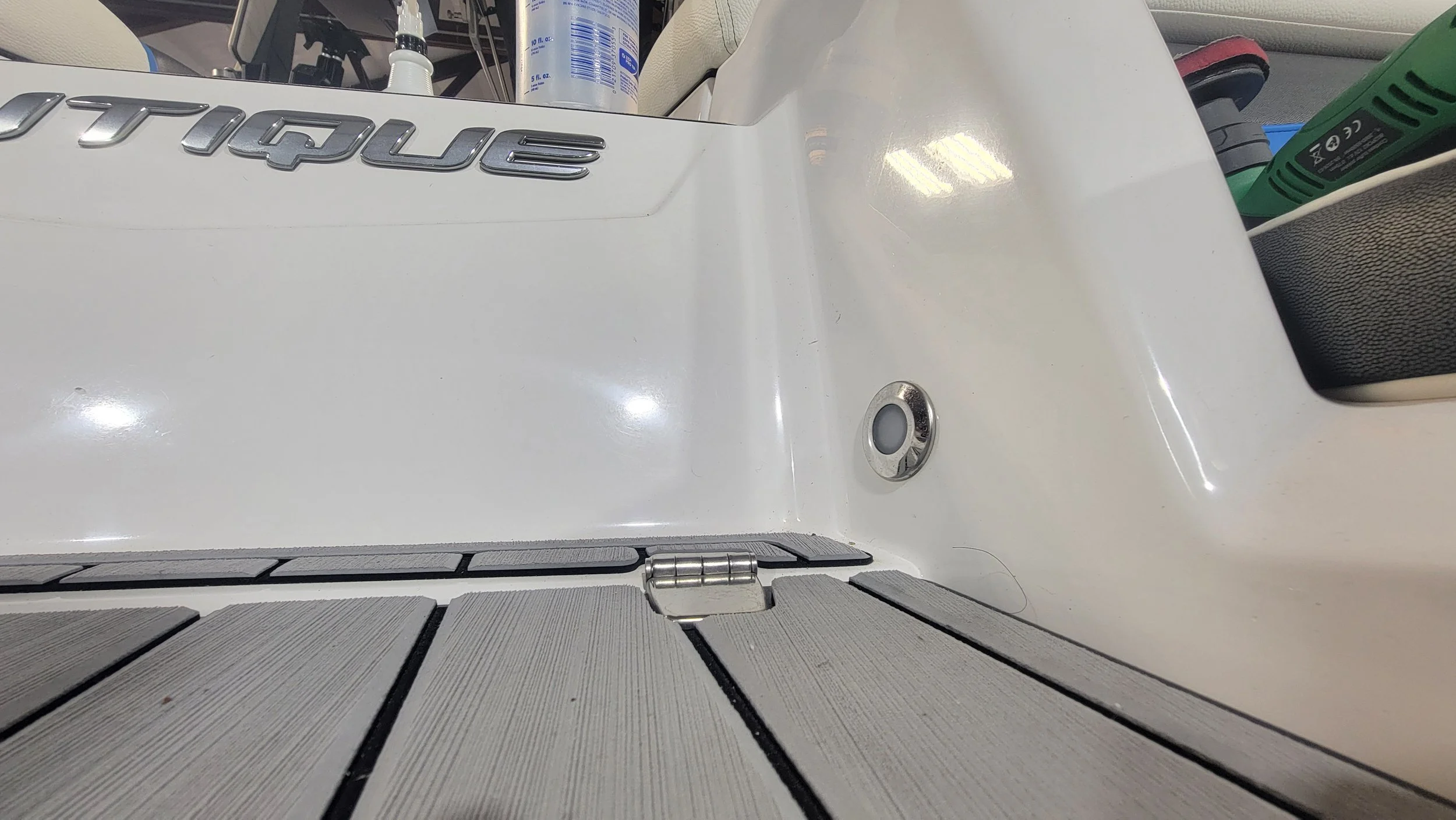 Close-up of a white boat hatch with chrome hardware, gray textured deck panels, and a raised chrome “EQUIP” emblem.