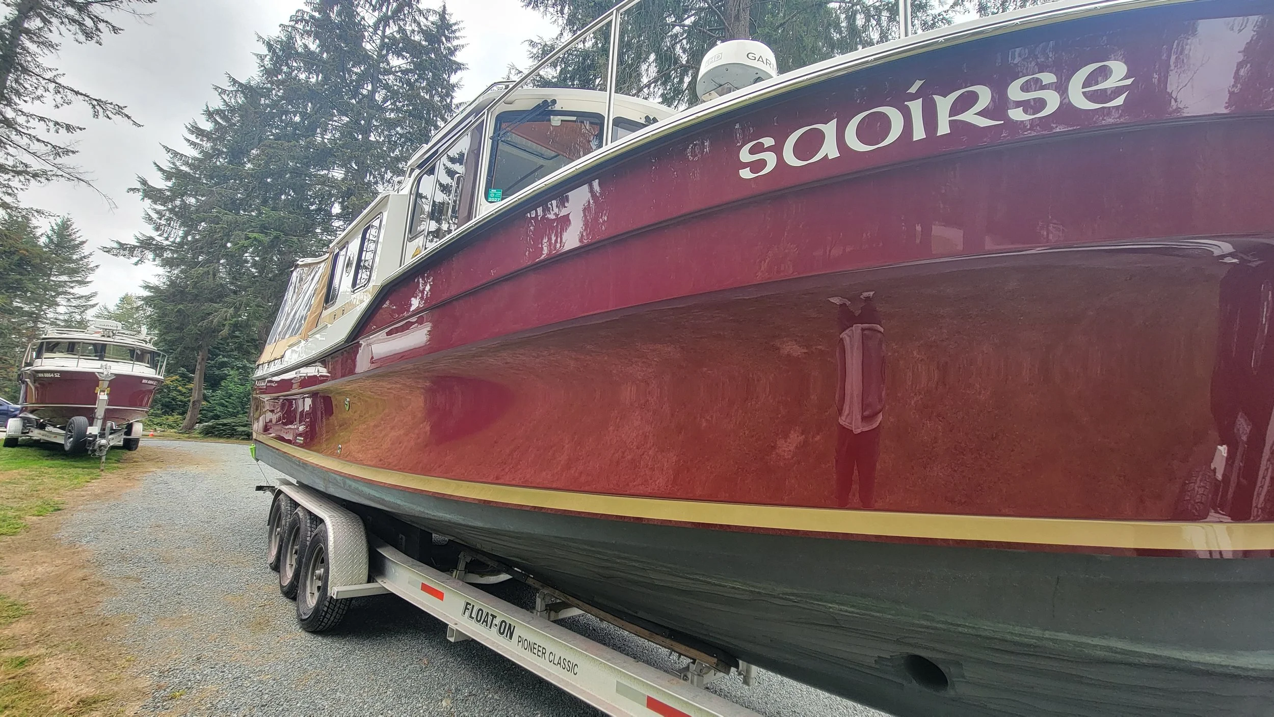 Maroon cabin cruiser named “Sploirse” on a trailer, with another boat parked among evergreen trees.