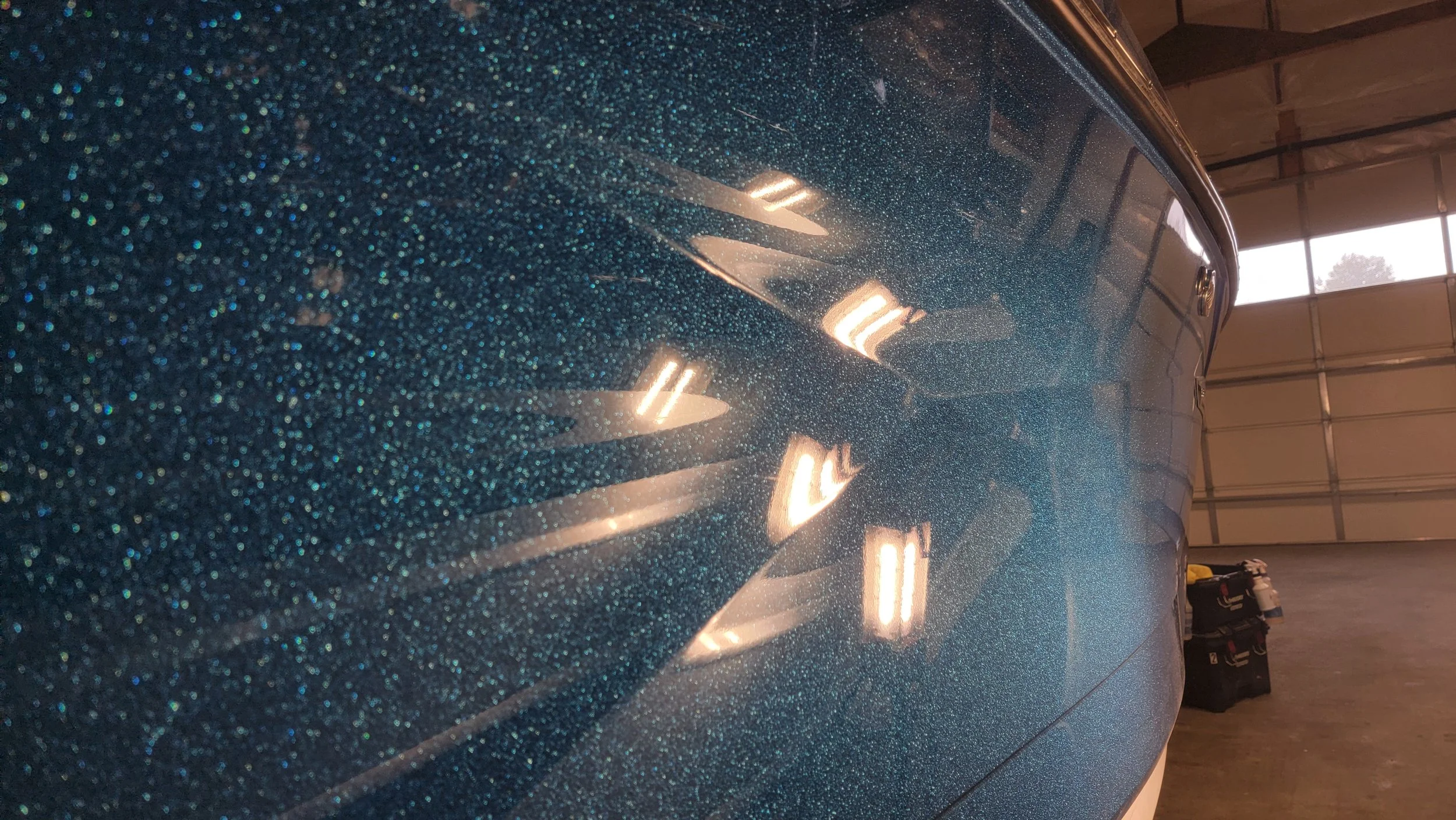 Close-up of a blue metallic airplane fuselage with rivets and reflected hangar lights inside an aircraft hangar