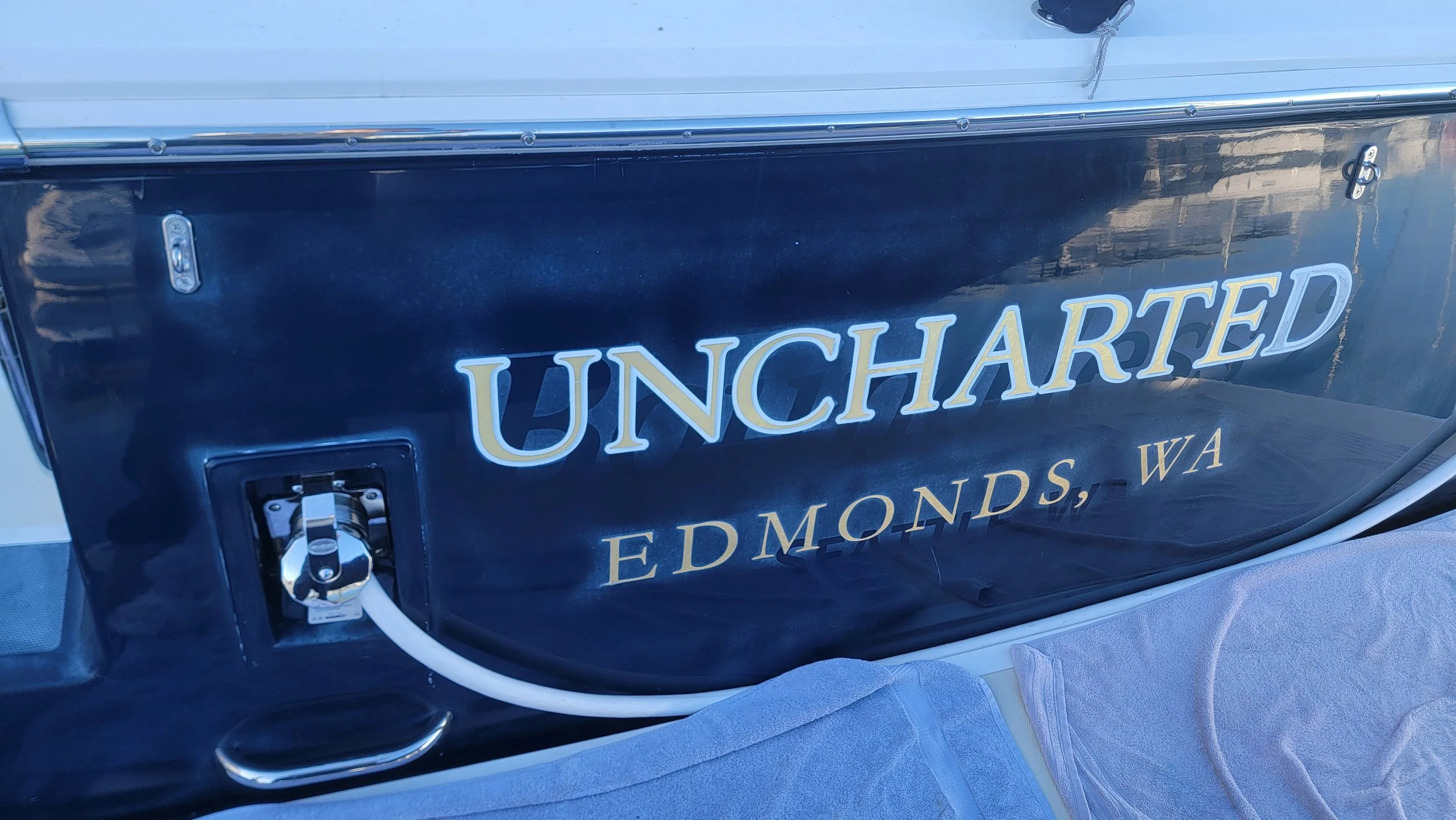 Close-up of a vintage dark blue boat with gold lettering reading “UNCHARTED” and “Edmonds, WA.”