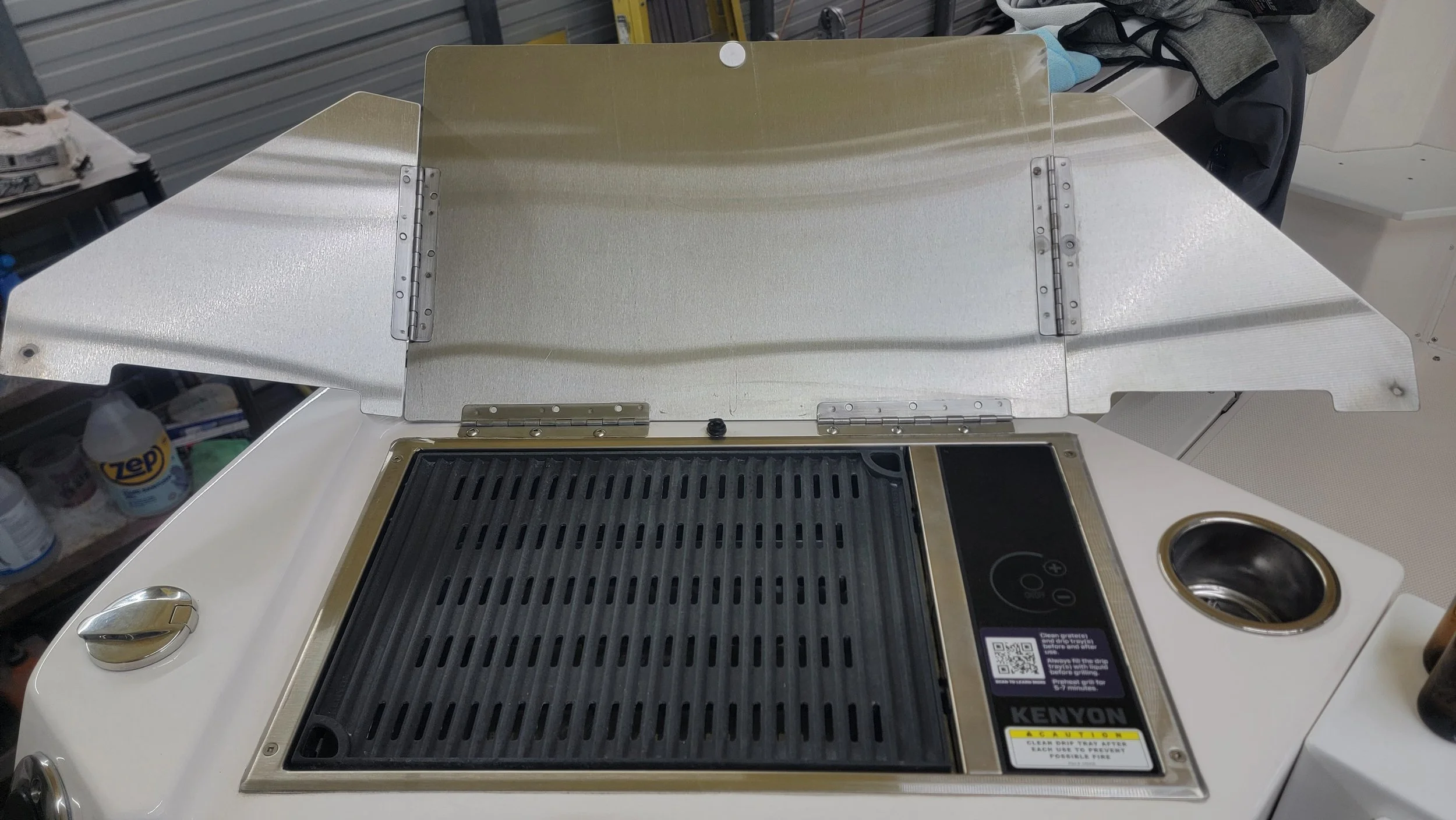 Open Kenyon electric grill with raised metal lid, black grill grate, controls, and drain cup.
