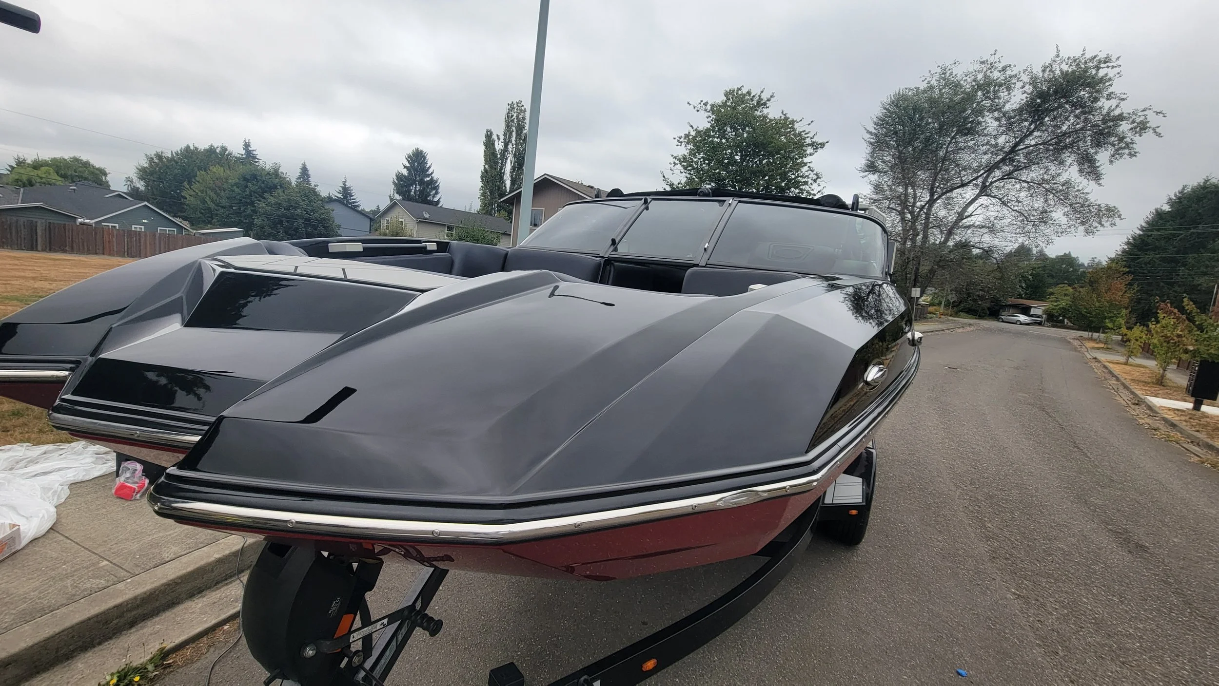 Black and burgundy motorboat on a trailer parked on a residential street.
