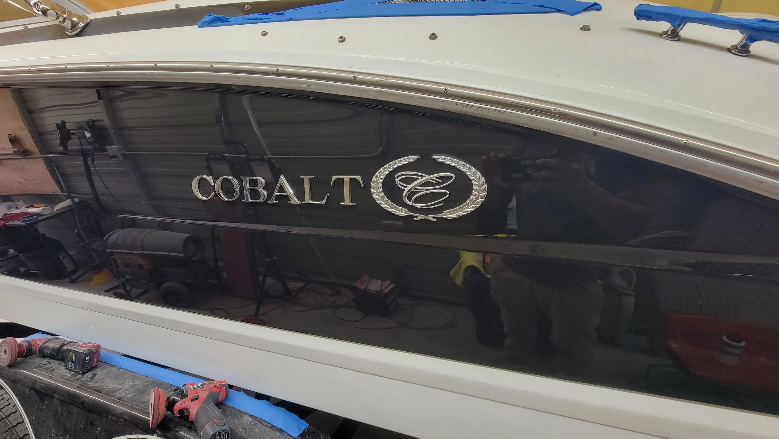 Close-up of a black-and-white Cobalt boat hull with chrome trim, Cobalt logo, and blue painter’s tape in a workshop