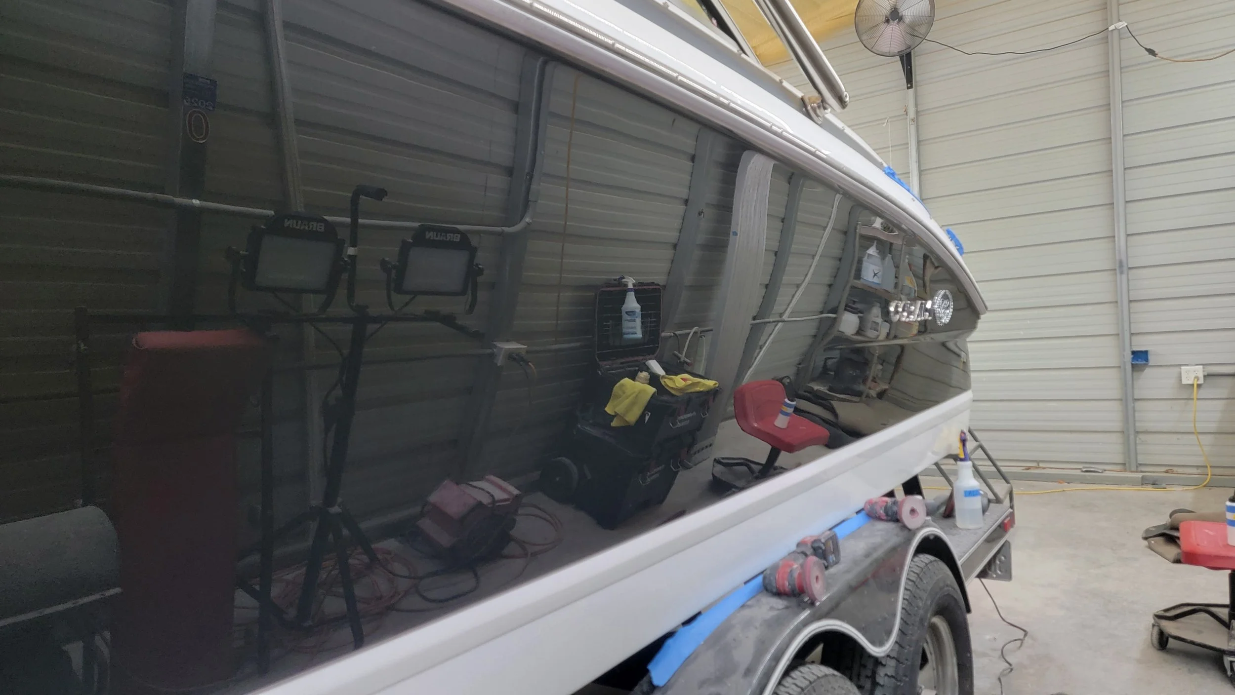 White motorboat being detailed in an industrial workshop with cleaning supplies and tools visible through the windshield