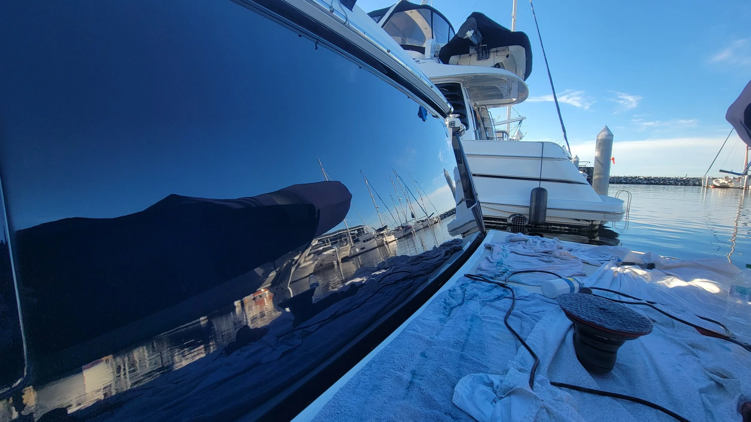 View from a boat deck of a marina with a neighboring motorboat, calm water, dock pilings, and clear blue sky
