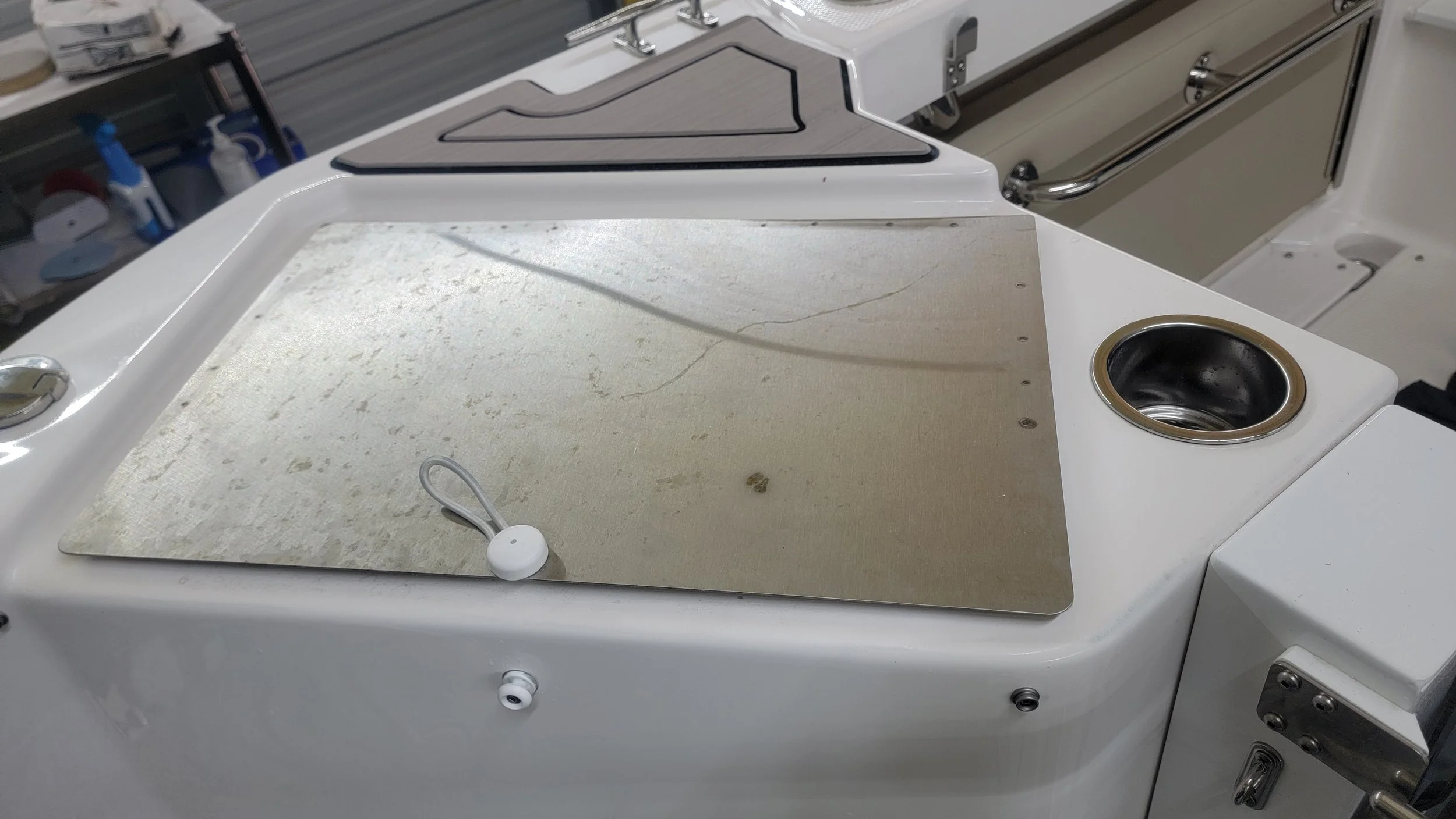 White boat deck with a large weathered metal panel, cup holder, railings, and marine hardware