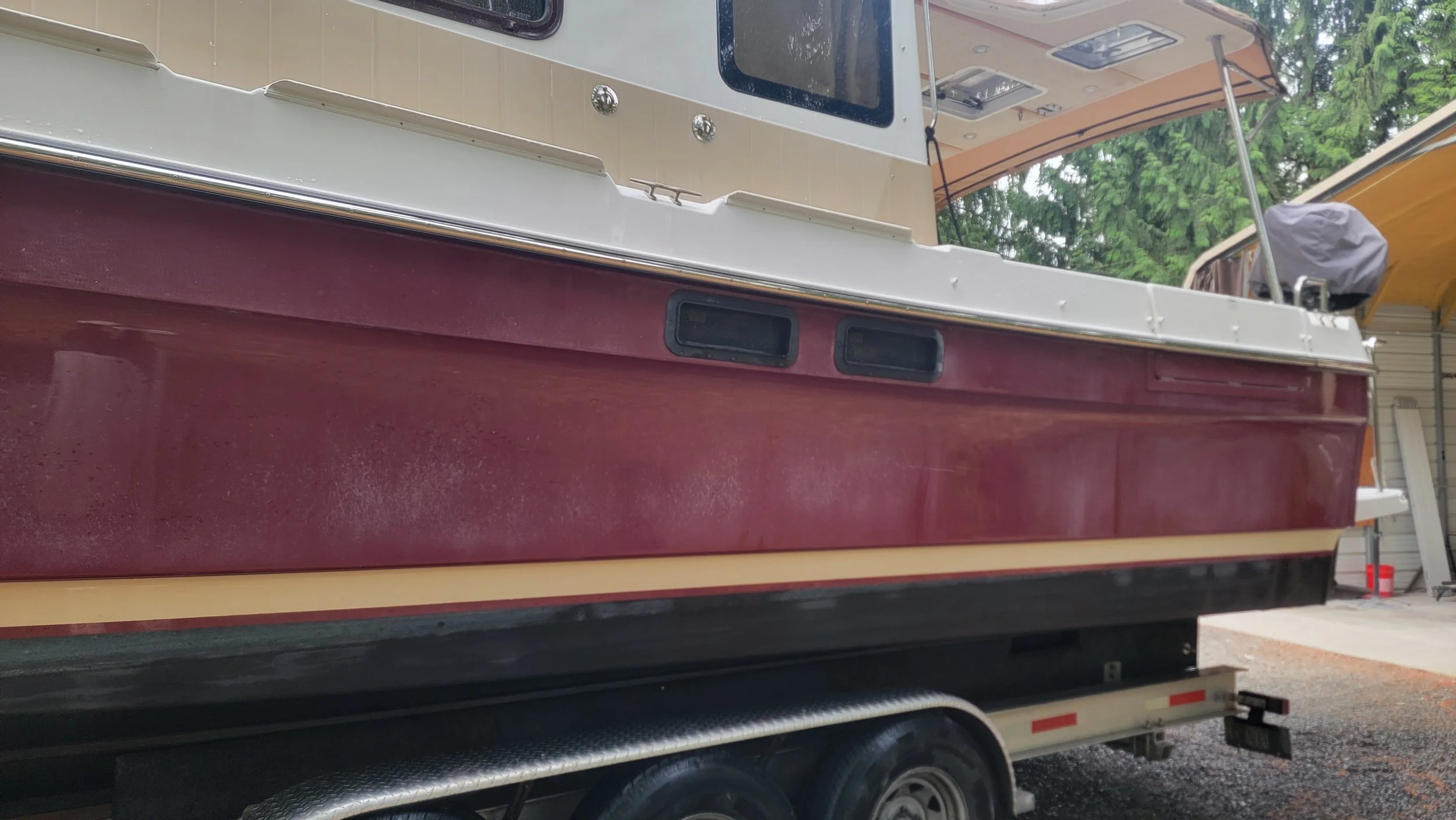 Maroon and white cabin boat mounted on a trailer outside a covered boat shelter