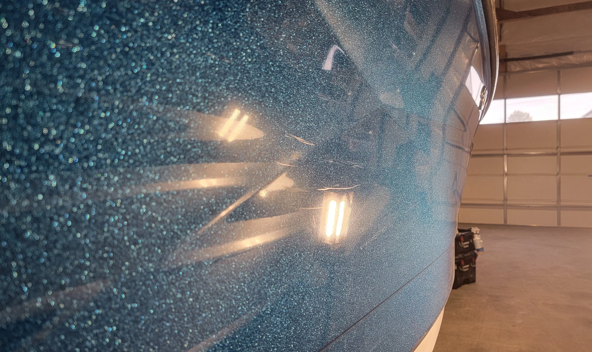 Close-up of a blue glitter-speckled vehicle or aircraft body reflecting overhead lights inside a hangar