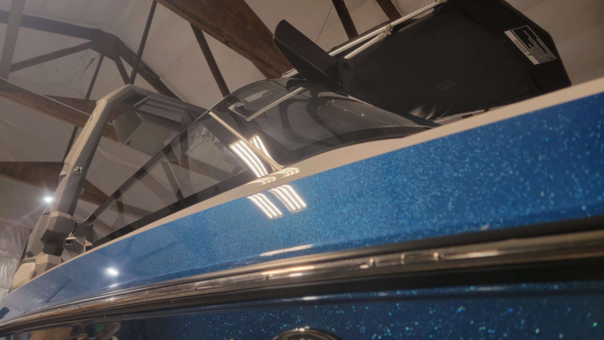 Close-up of a blue glittery vintage car with chrome trim and its open hood indoors.