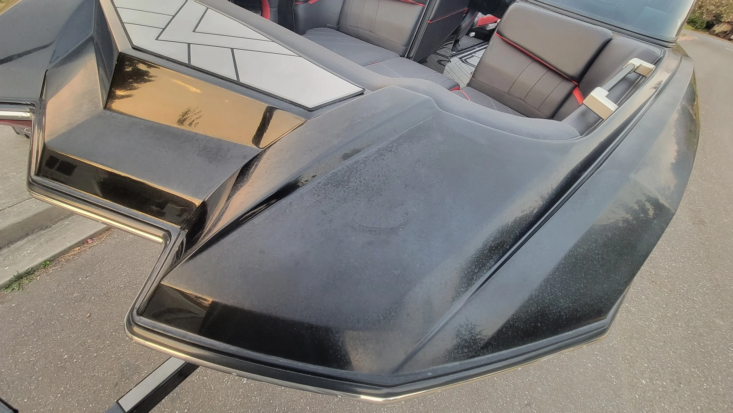 Close-up of a black custom convertible car with angular bodywork, gray leather seats, red trim, and chrome accents.