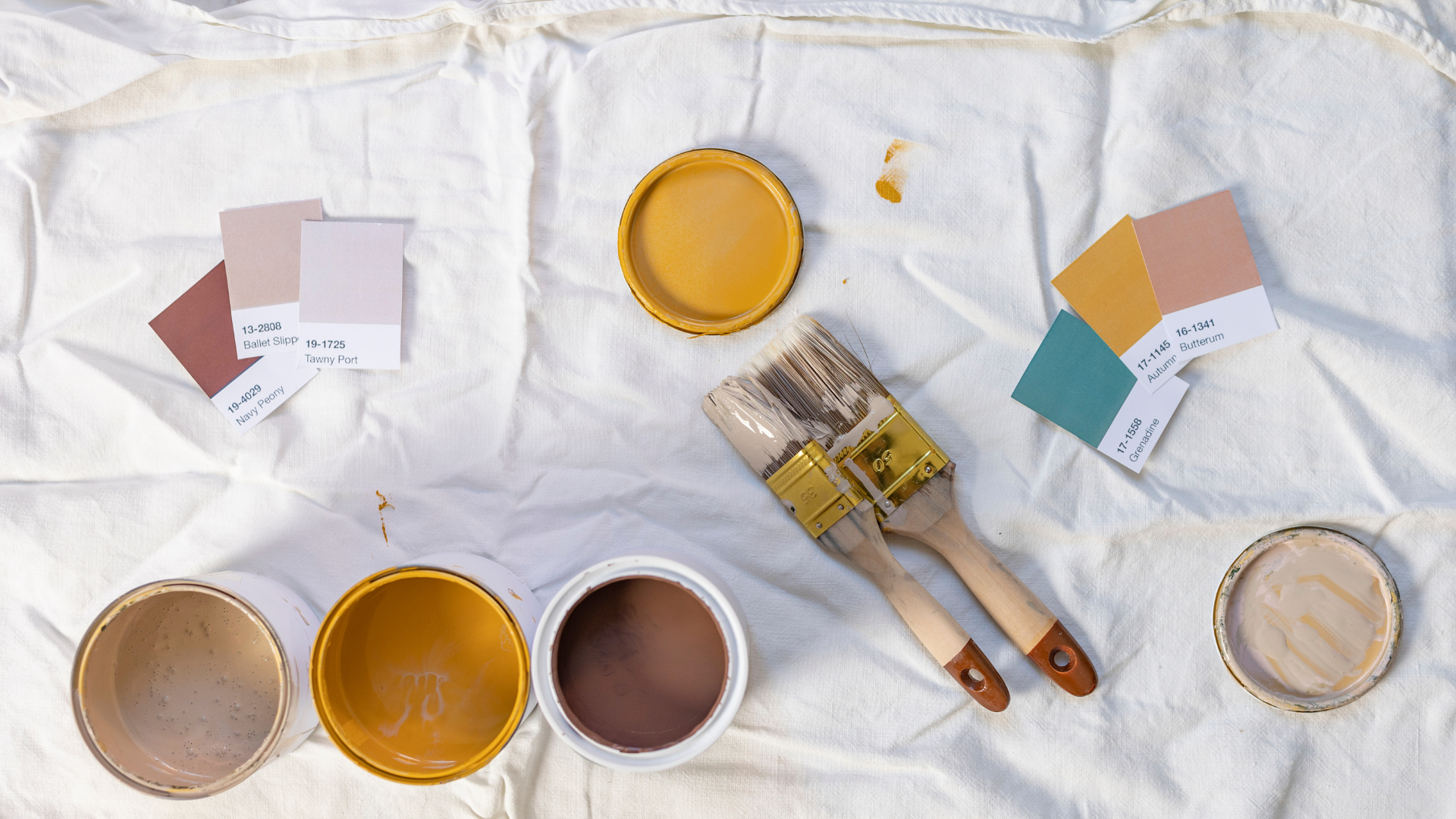 Top-down view of paint cans, brushes, paint swatches, and spilled paint on a white cloth