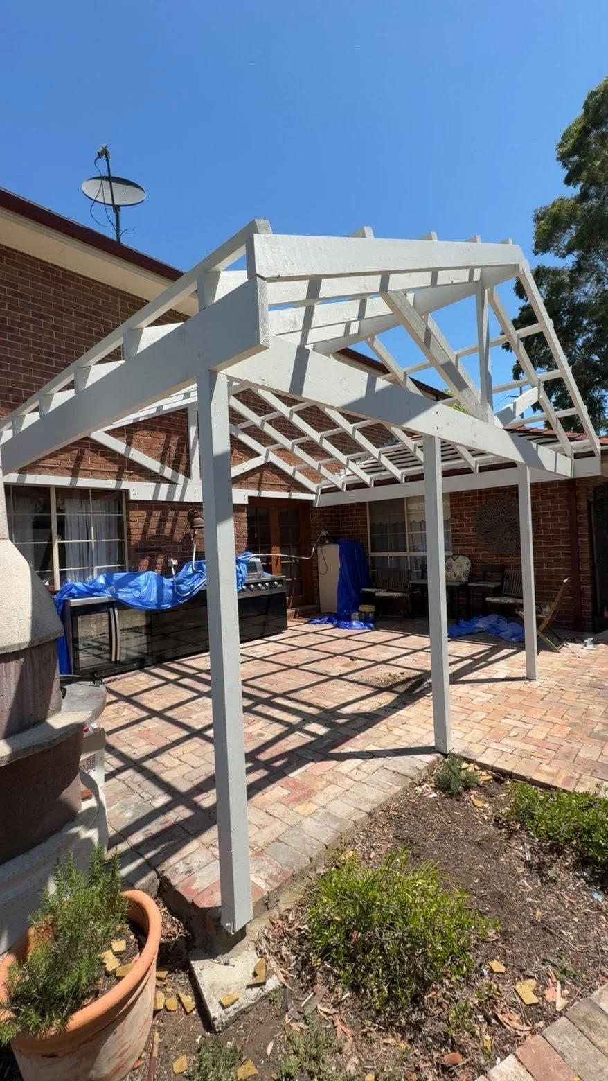 White-painted wooden pergola over a brick-paved backyard patio beside a brick house