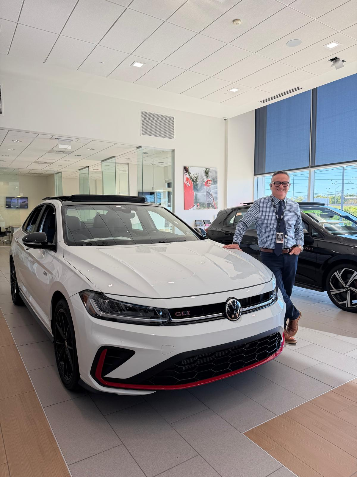 Hernan “H” Diaz-Egg beside a white Volkswagen GLI at Autohaus Lancaster