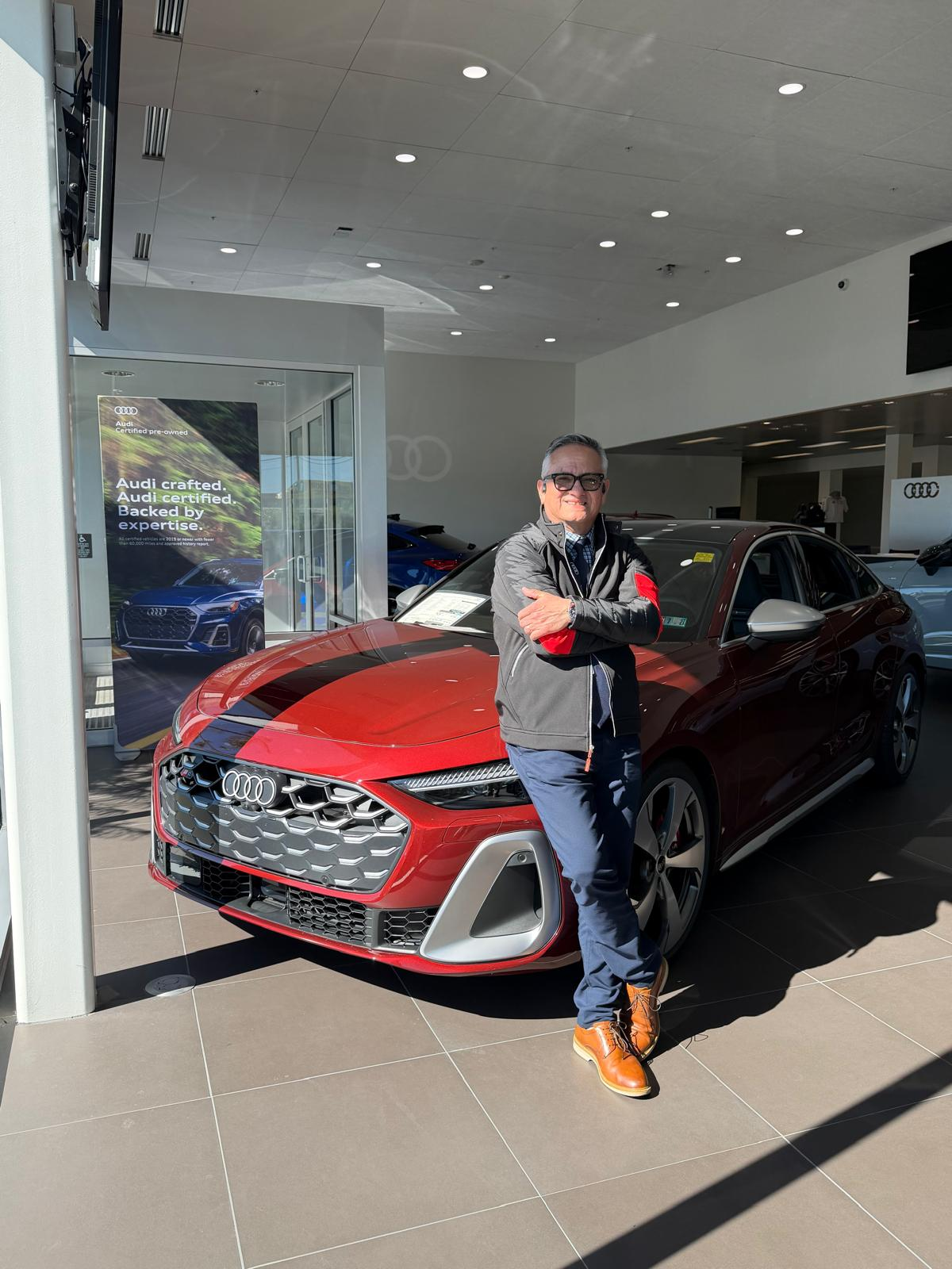 Hernan “H” Diaz-Egg beside a red Audi in the Autohaus Lancaster showroom