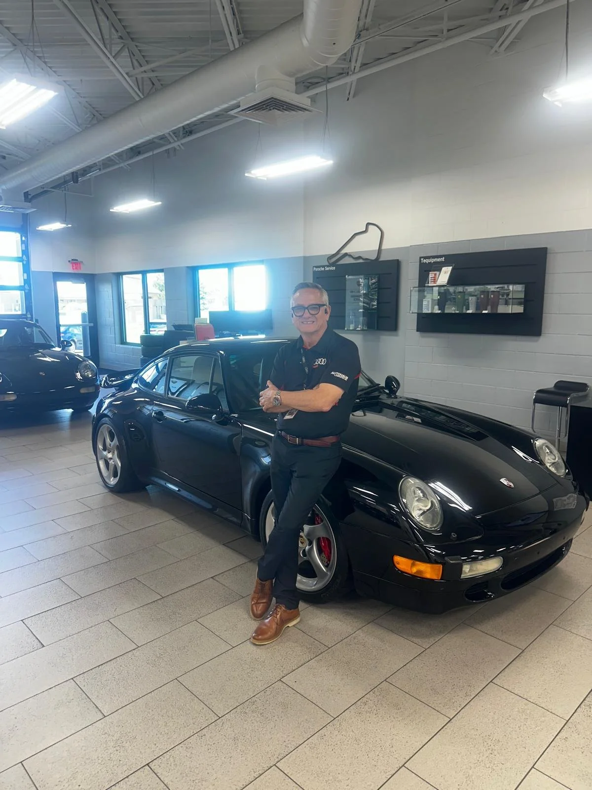 Hernan “H” Diaz-Egg beside a black Porsche at Autohaus Lancaster