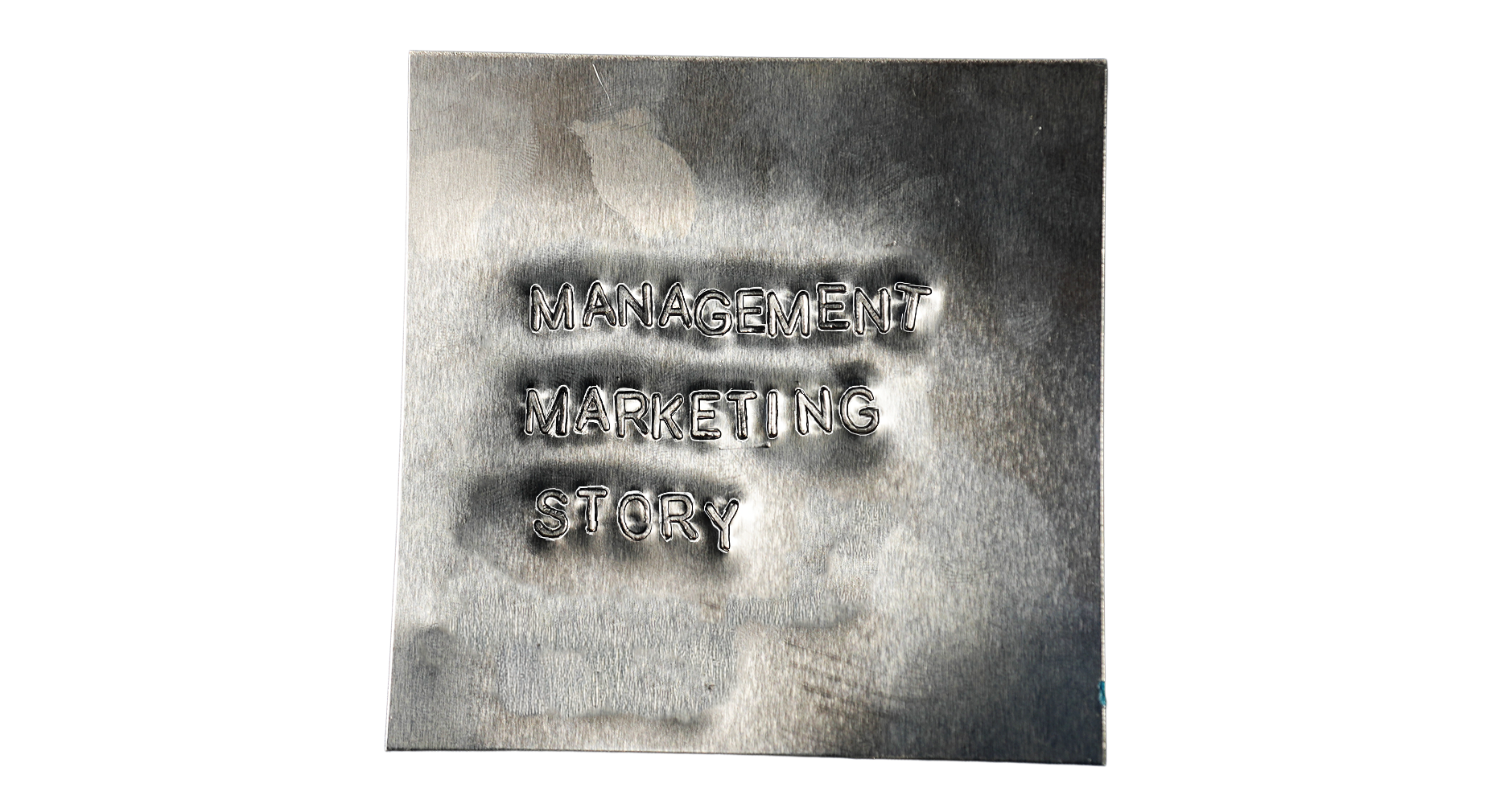 A metallic plaque with engraved words 'Management Marketing Story' on a dark background.
