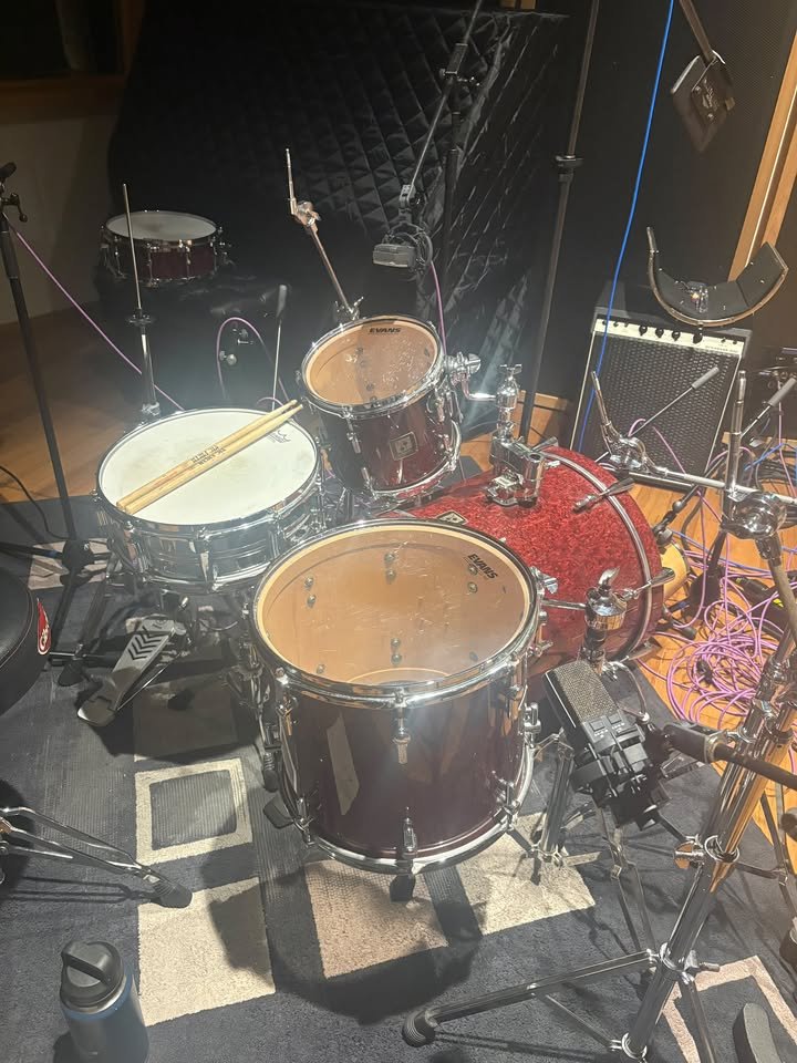A drum set in a recording studio with microphones and equipment surrounding it.