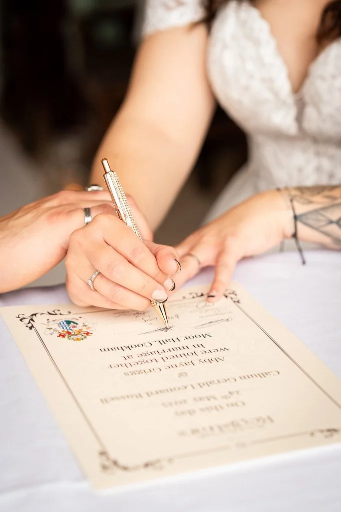 A person signing a certificate with a decorative border and an official crest, possibly at a wedding or official event.