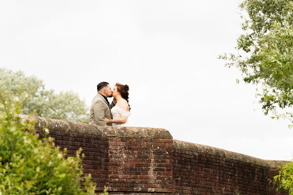 A couple sharing a kiss on a brick bridge surrounded by greenery.