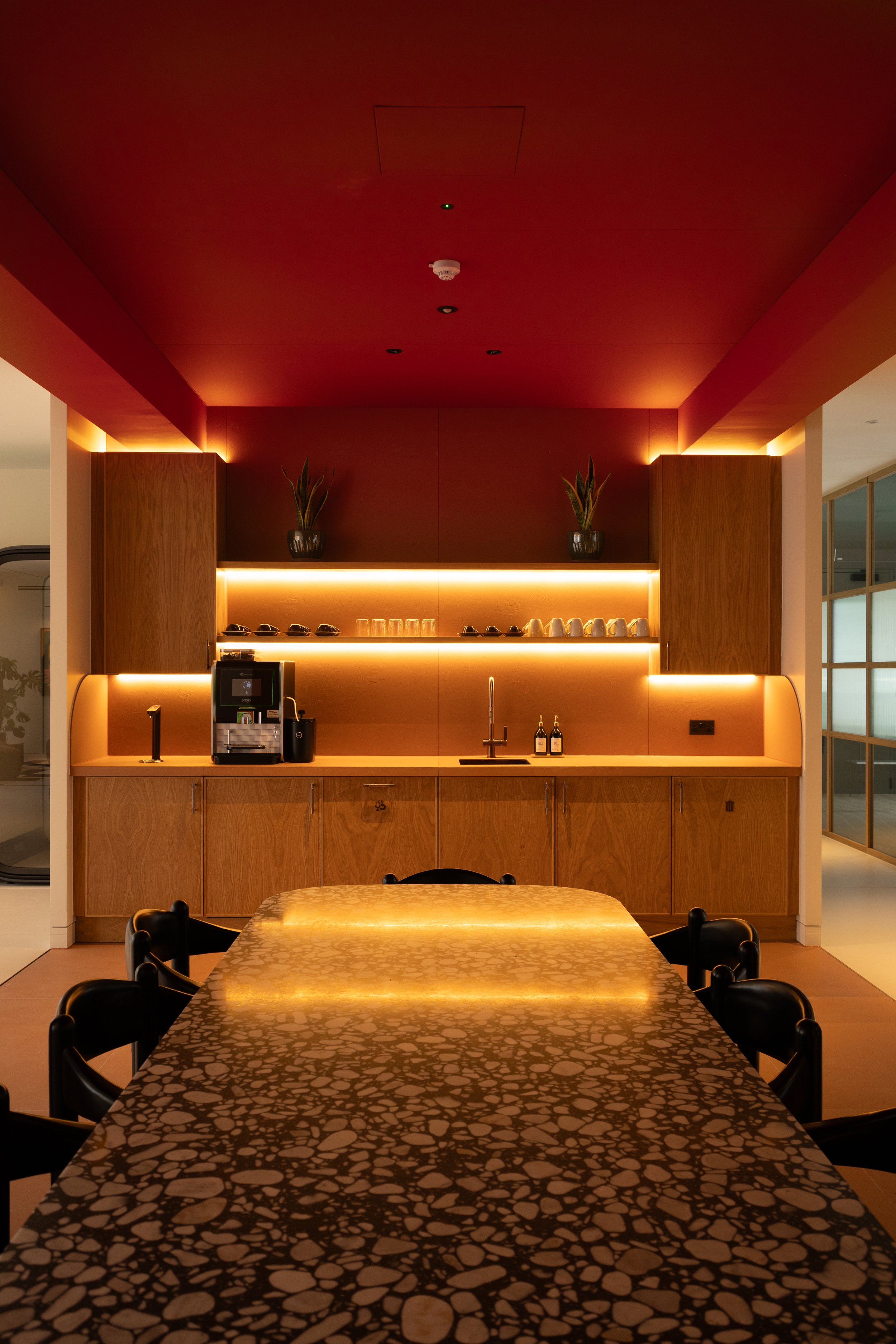 A modern kitchen and dining area with a dark red ceiling, wooden cabinets, and a patterned black and gold table with black chairs.