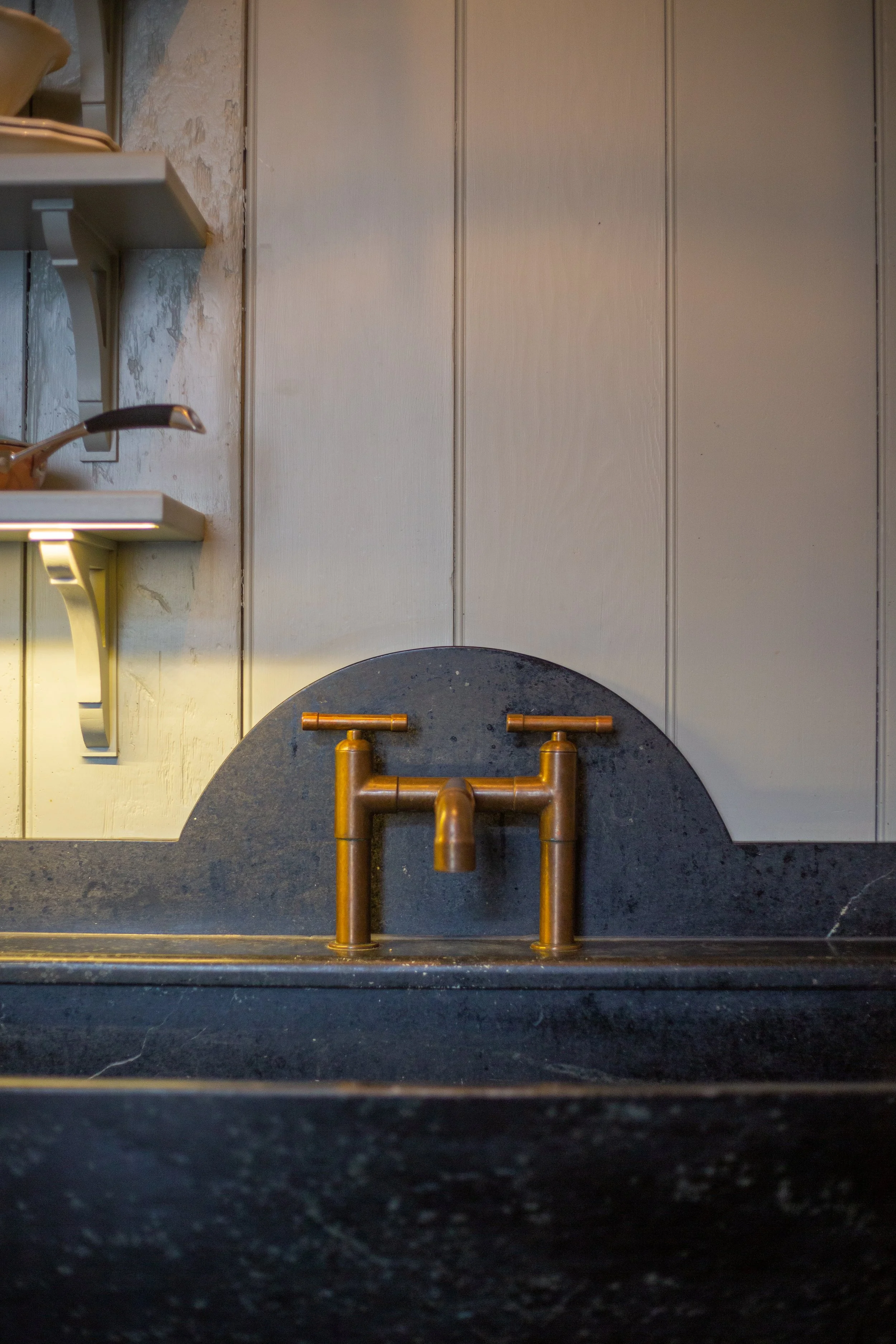 Close-up of a black kitchen sink with a copper faucet, dark countertop, and beige wooden wall paneling in the background.