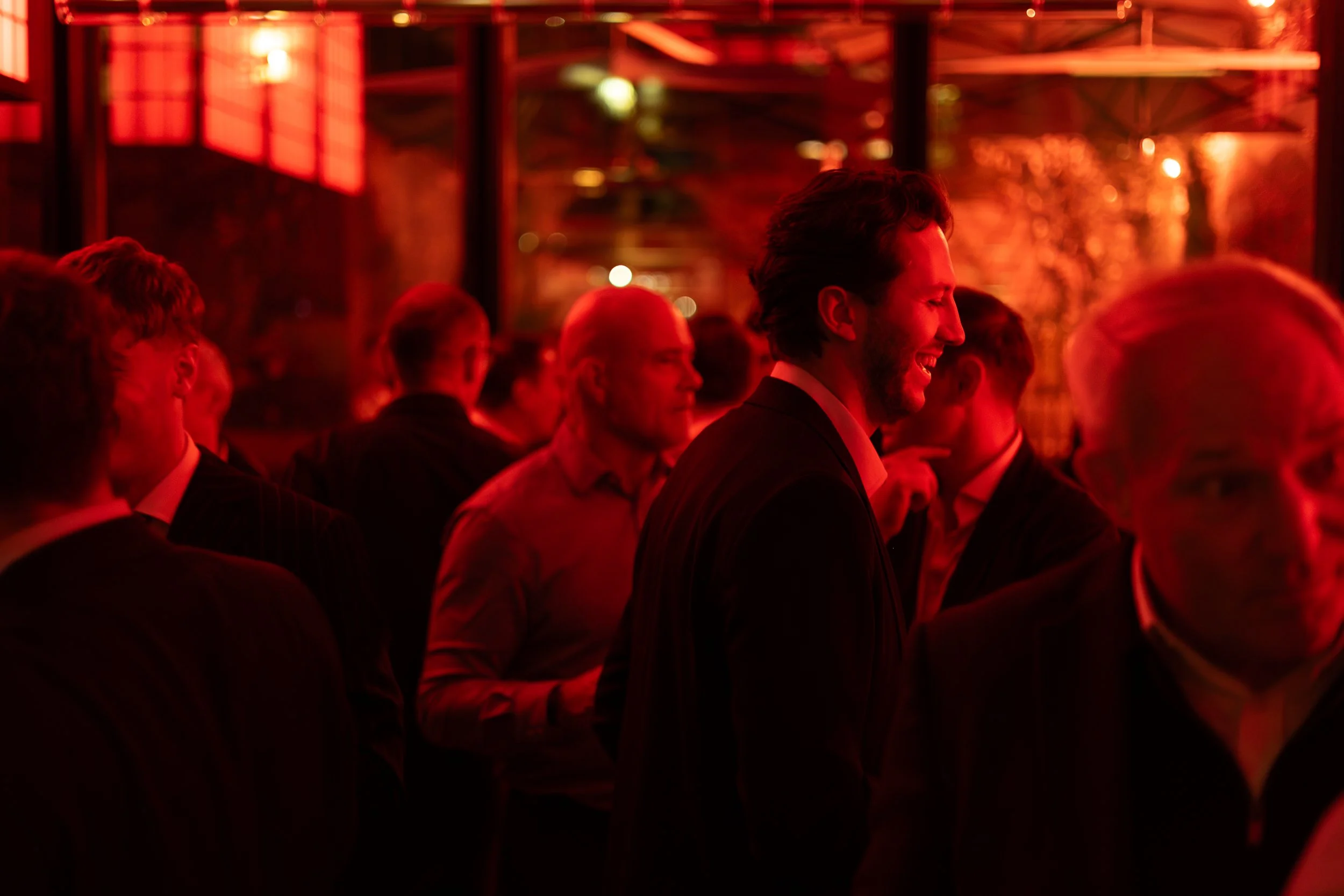 People dressed in formal attire attending an event with red lighting and warm ambiance.