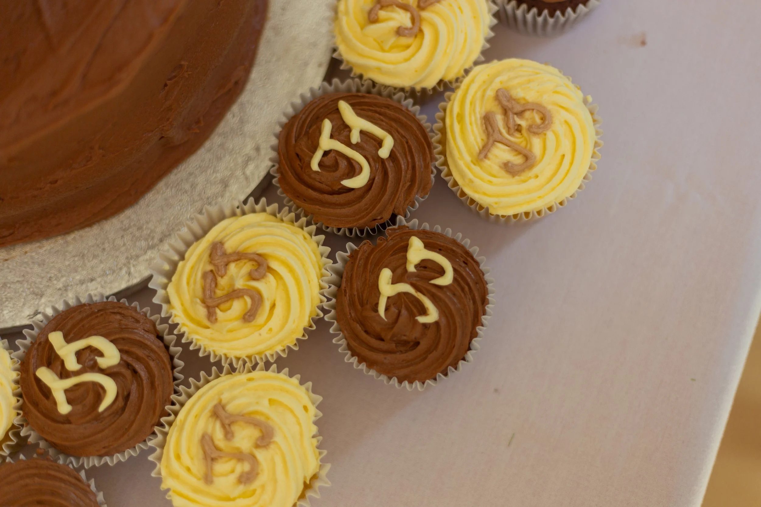 Cupcakes with yellow and brown swirled frosting, some decorated with small chocolate or vanilla sprinkles, on a white surface.