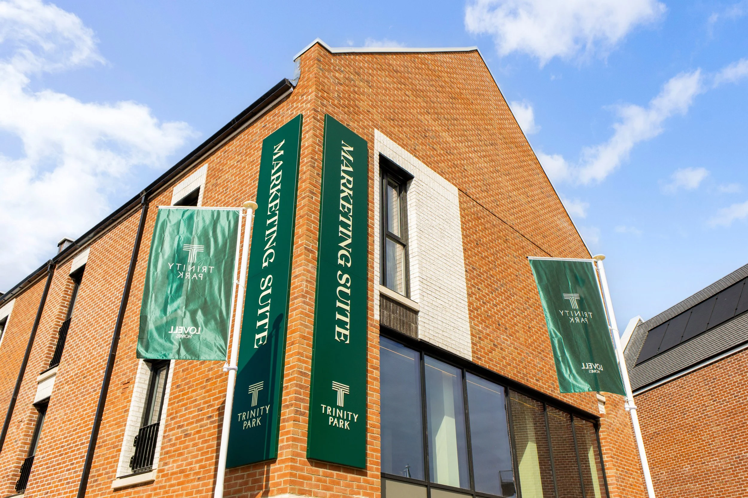 External view of a brick building with multiple green banners reading 'Trinity Park' and 'Sustainability.'