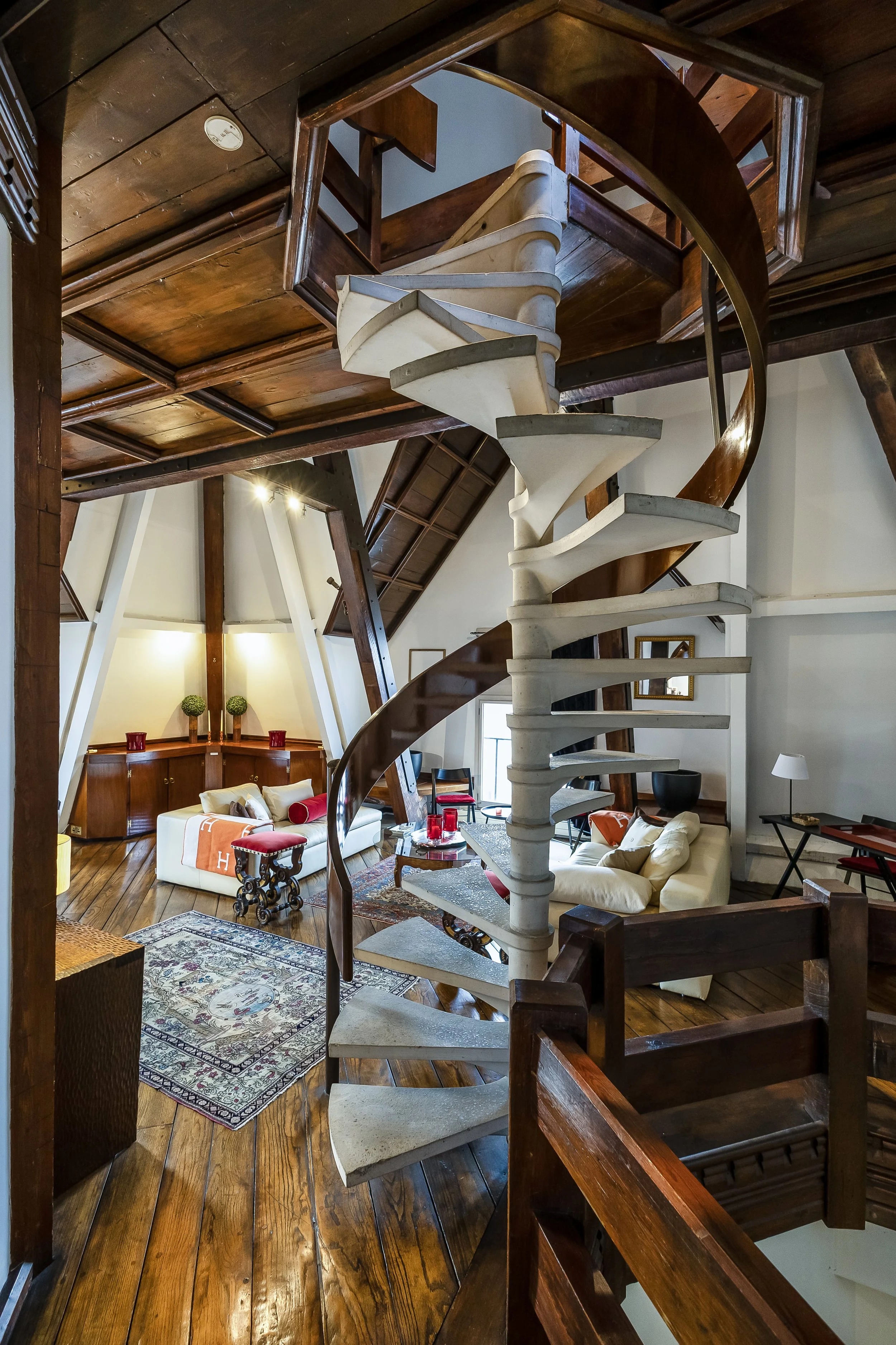 Interior of a house showcasing a spiral staircase, wooden floors, and a seating area with sofas, artwork, and decorative items.