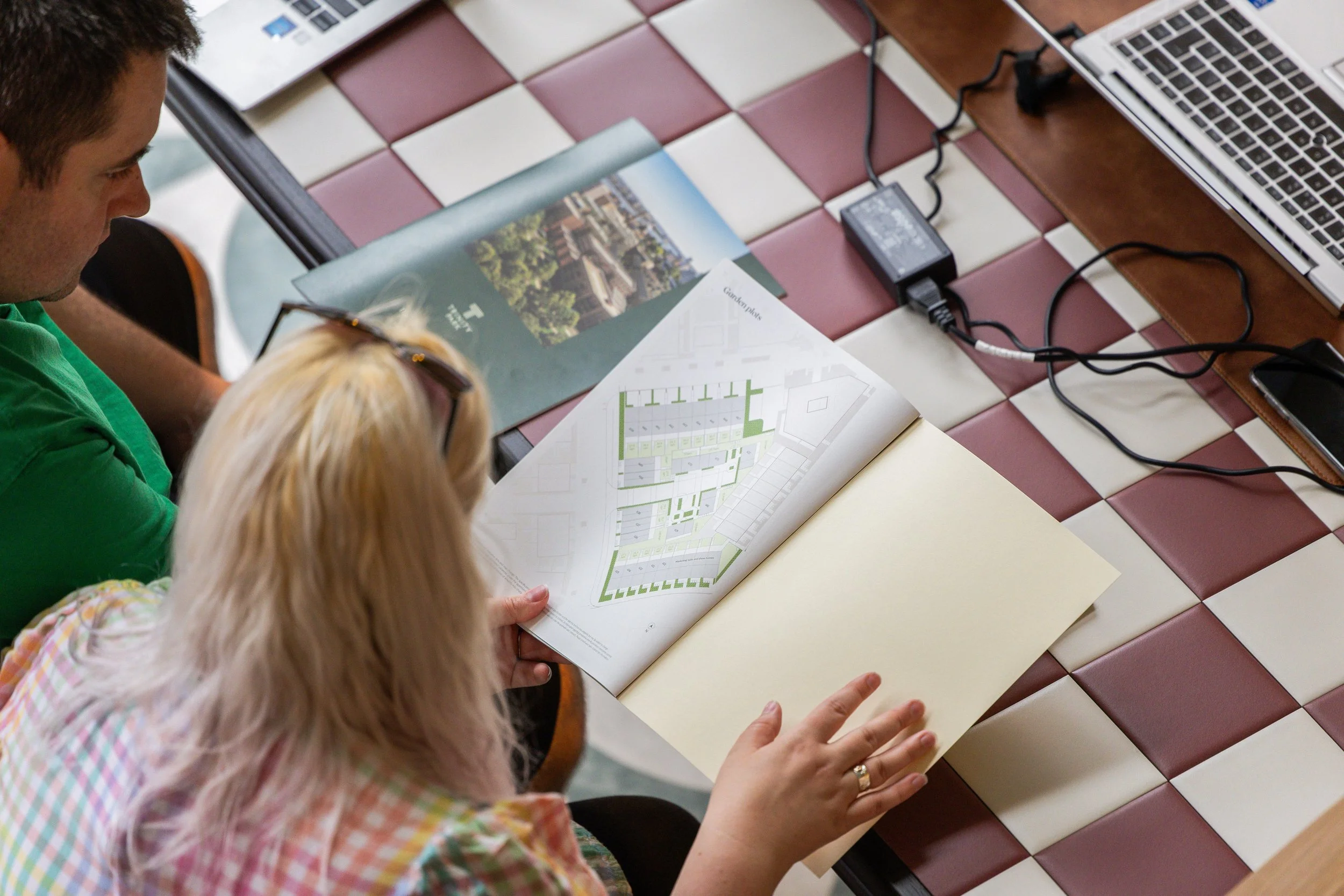 People sitting at a table with maps, pamphlets, and electronic devices, possibly reviewing travel or city planning materials.
