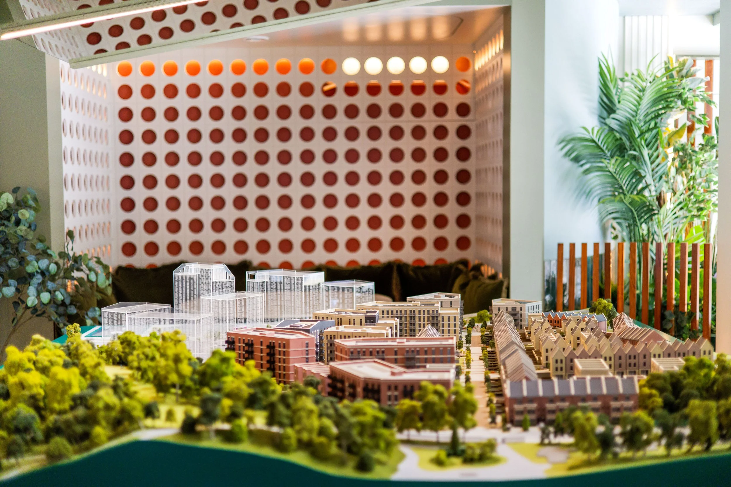 A detailed architectural model of a residential development, including miniature buildings, roads, and green spaces, displayed on a table with plants around it.