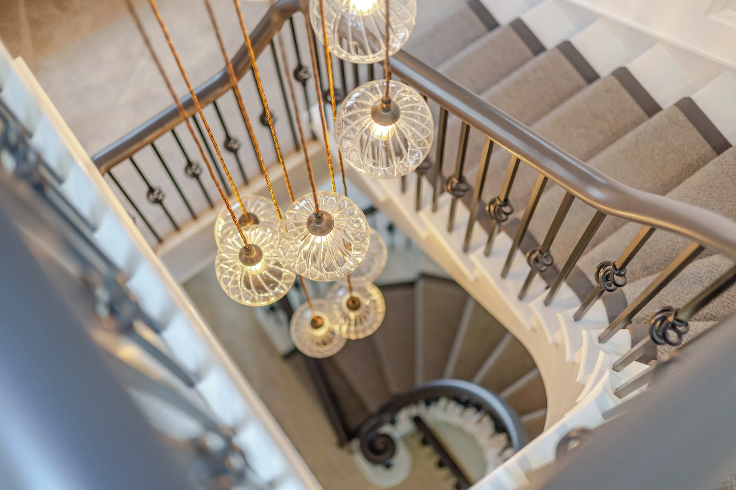 View of a staircase with hanging pendant lights and a metallic handrail.