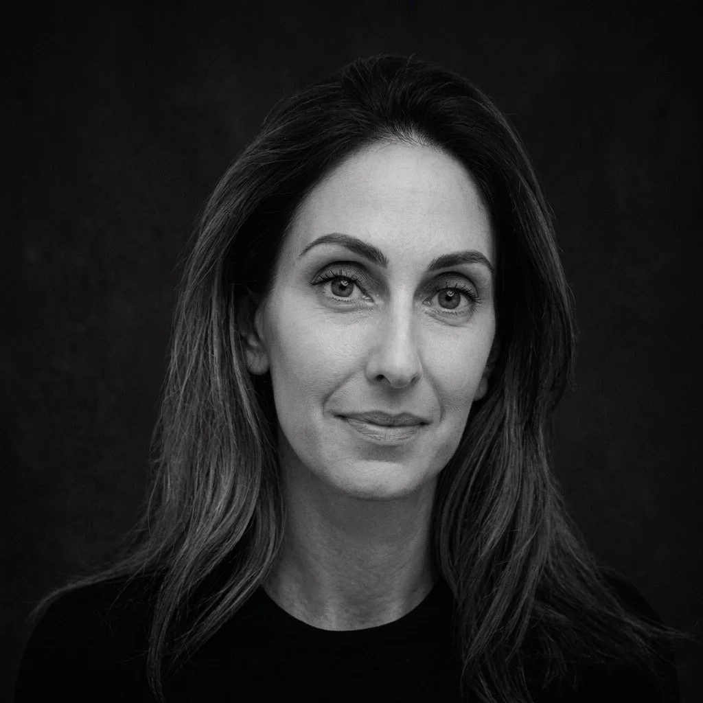 Black and white portrait of a woman with long wavy hair, looking at the camera with a slight smile, dark background.