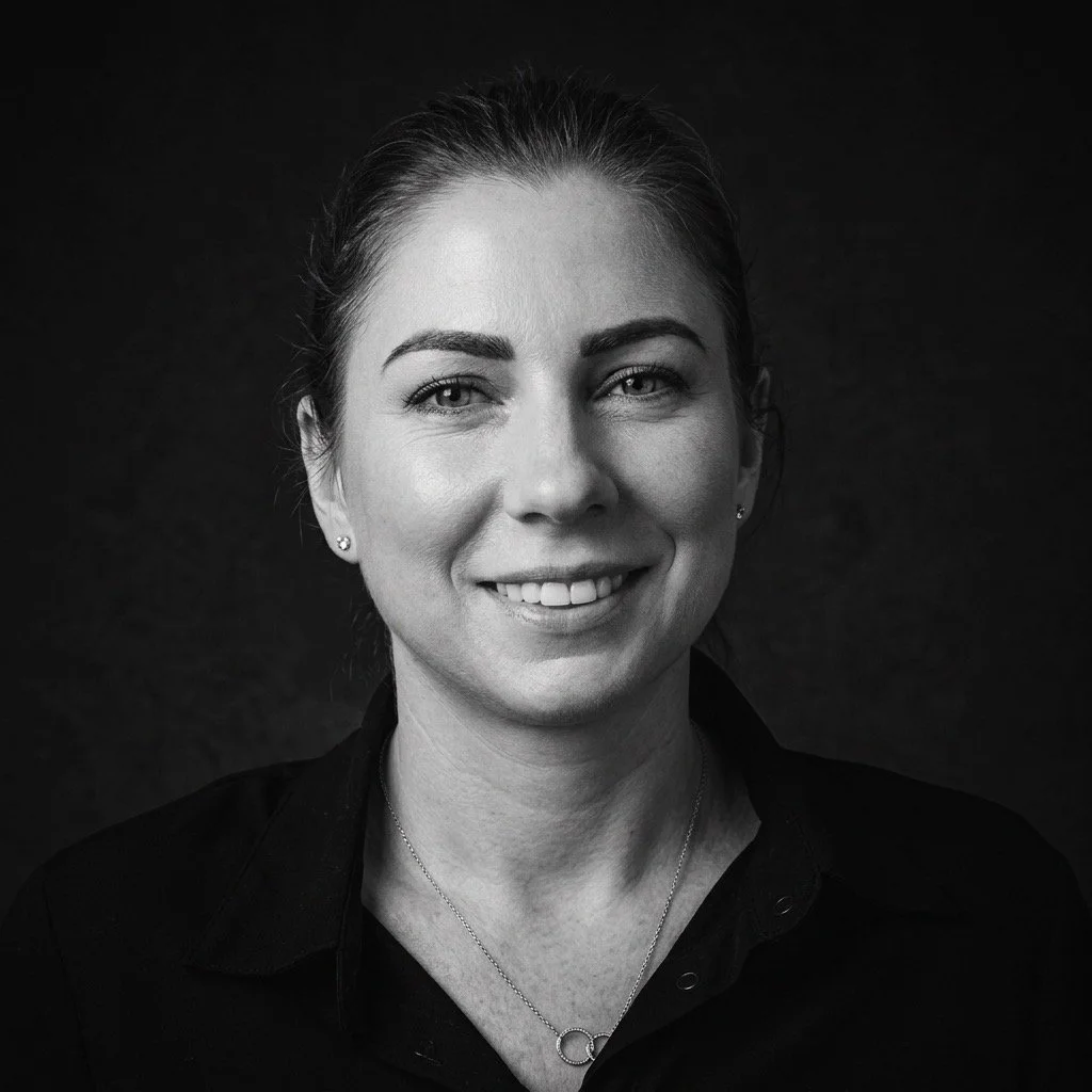 Black and white portrait of a woman smiling, with her hair pulled back, wearing a dark shirt and earrings.
