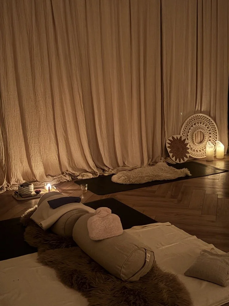 Cozy spa or massage room with dim lighting, a person lying face down on a massage table with a towel and kitchenette accessories nearby, candles, and decorative wall art. Yin yoga classes with luxury props and candlelit. 