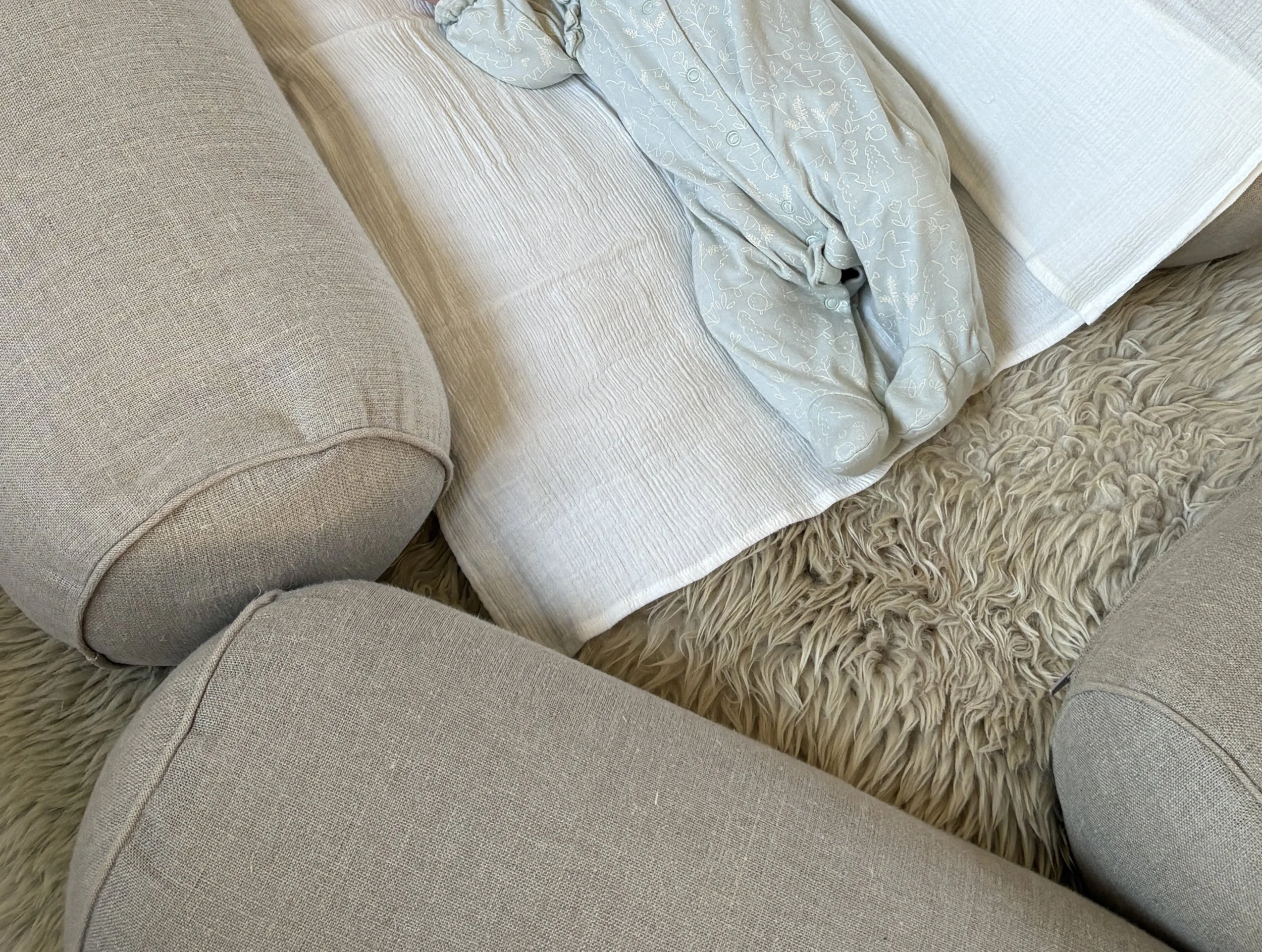 Close-up of beige upholstered furniture with a throw blanket and fluffy rug on the floor. Postnatal Mum and baby yoga. 