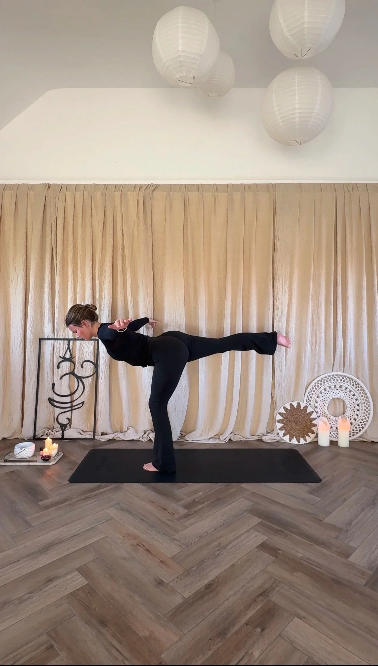 Person practicing yoga in a studio with candles, decorative items, and a beige curtain backdrop. Yoga embodiment somatics nervous system regulation, embodied flow. Somatic exercises. 